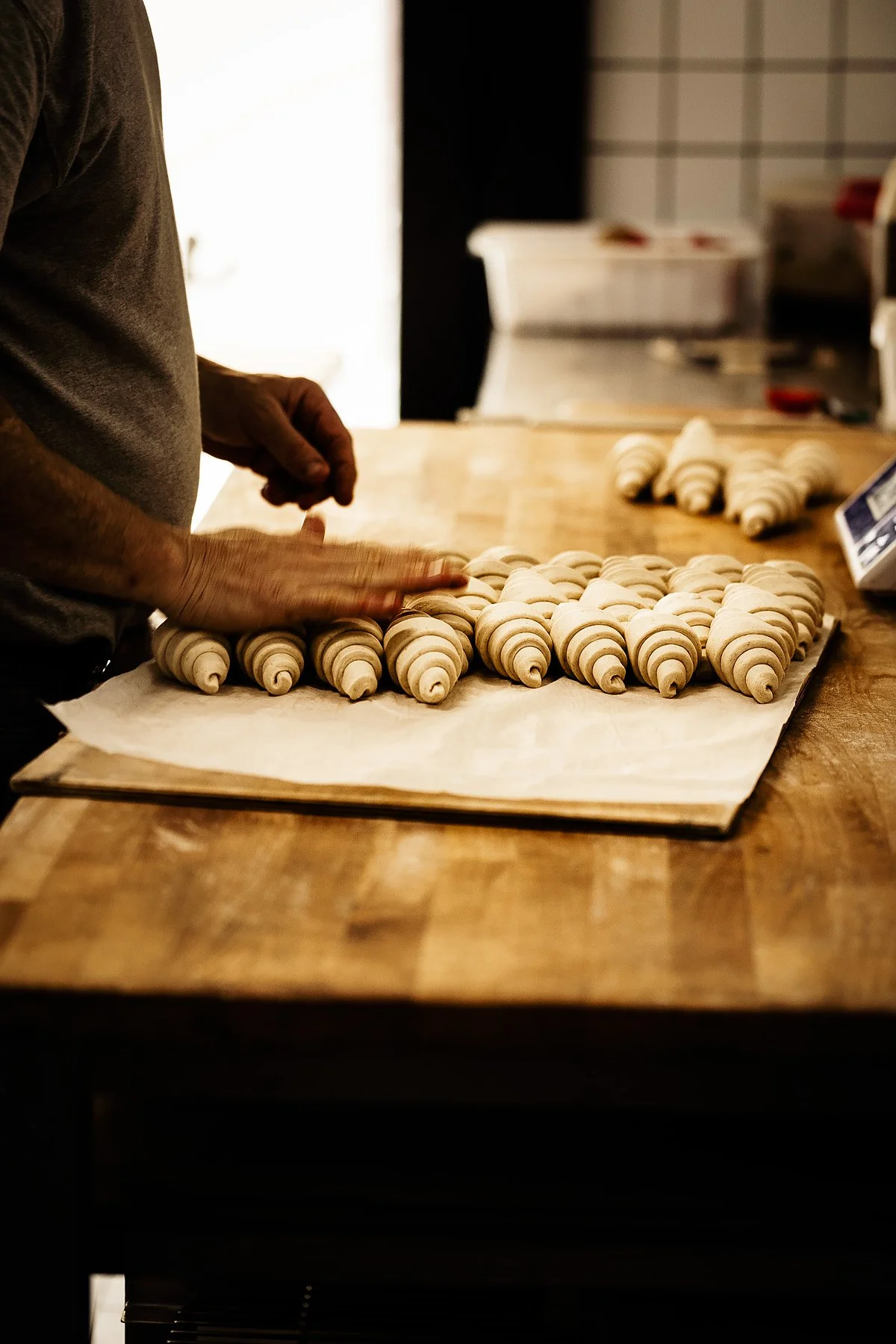 A person shaping croissants on a parchment paper-lined baking sheet in a kitchen.