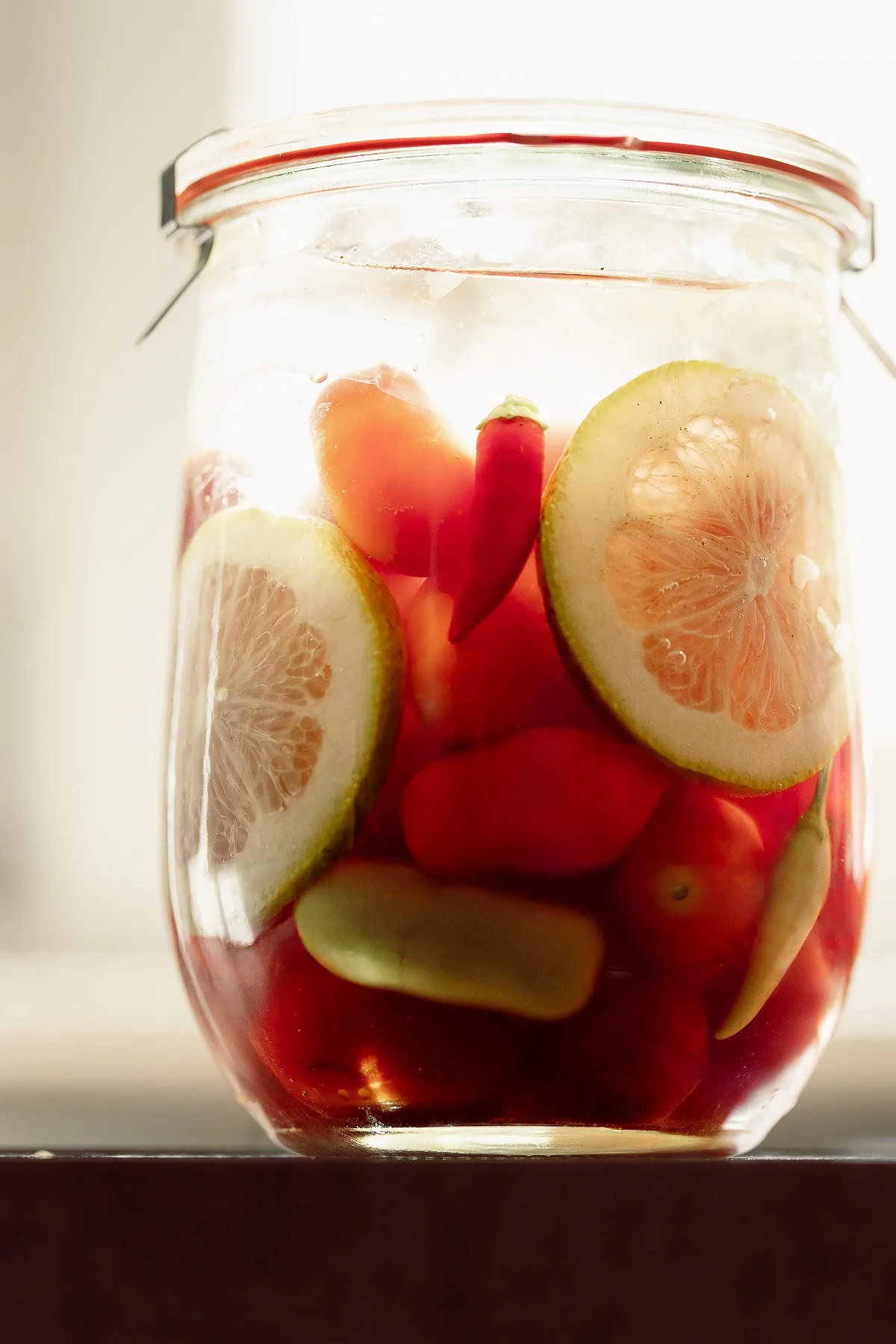 A glass jar filled with lemons and small red hot peppers.
