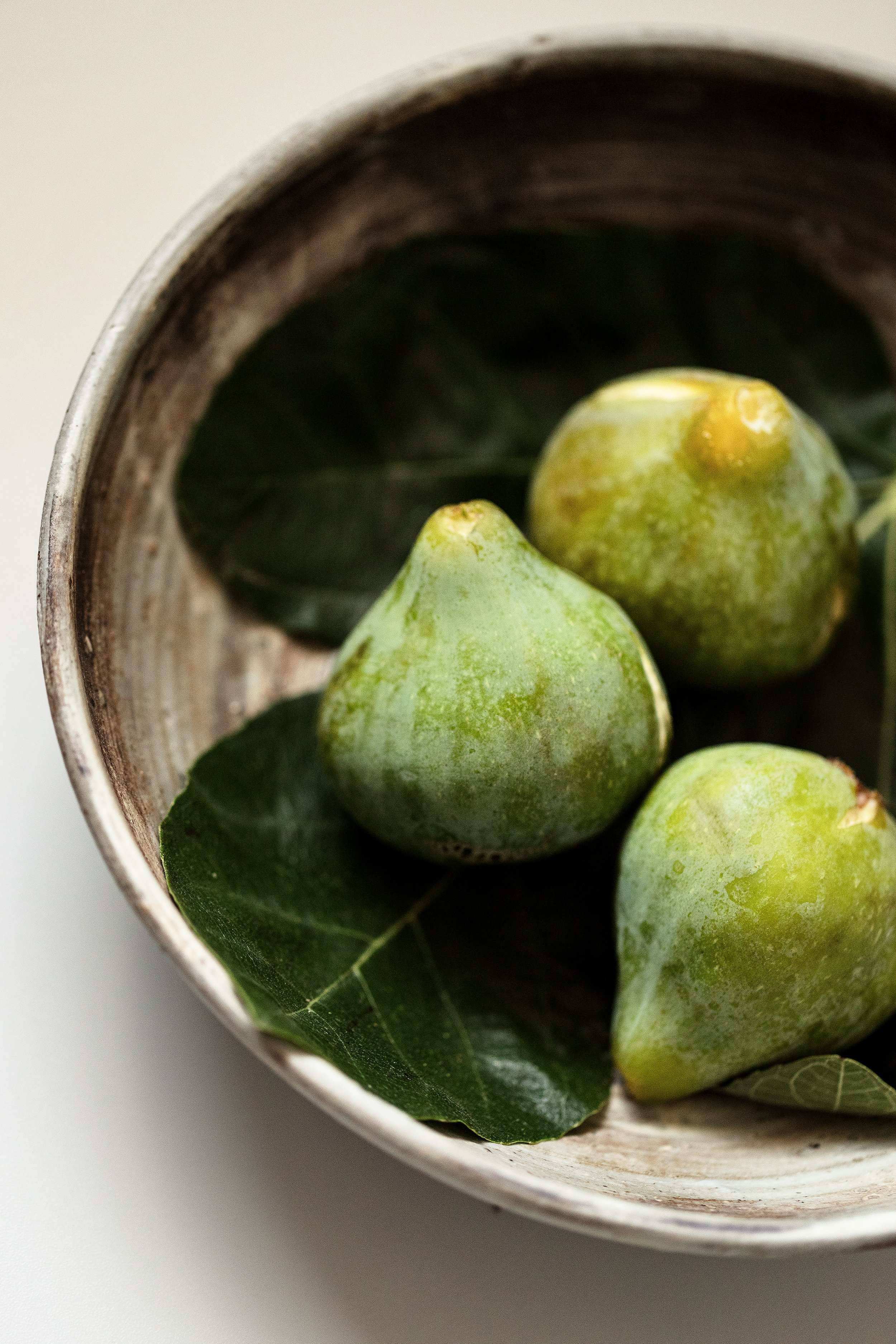 Close-up of green figs with leaves inside a rustic, silver bowl.