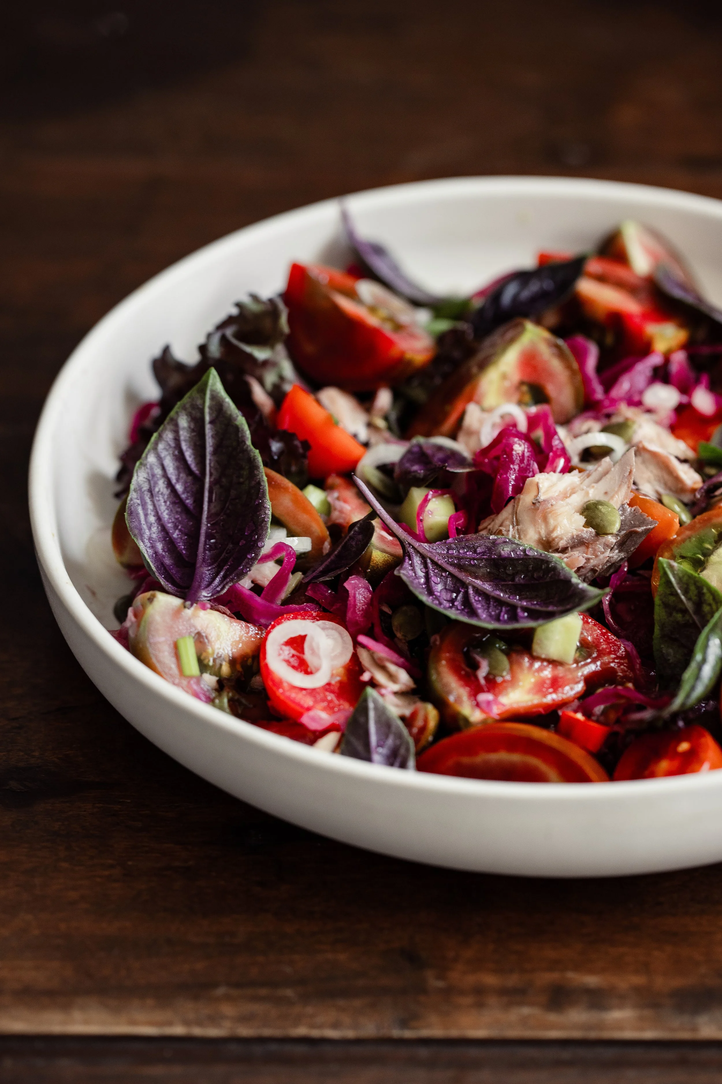 Bowl of fresh vegetable salad with tomatoes, red onions, and purple basil leaves on a wooden surface.