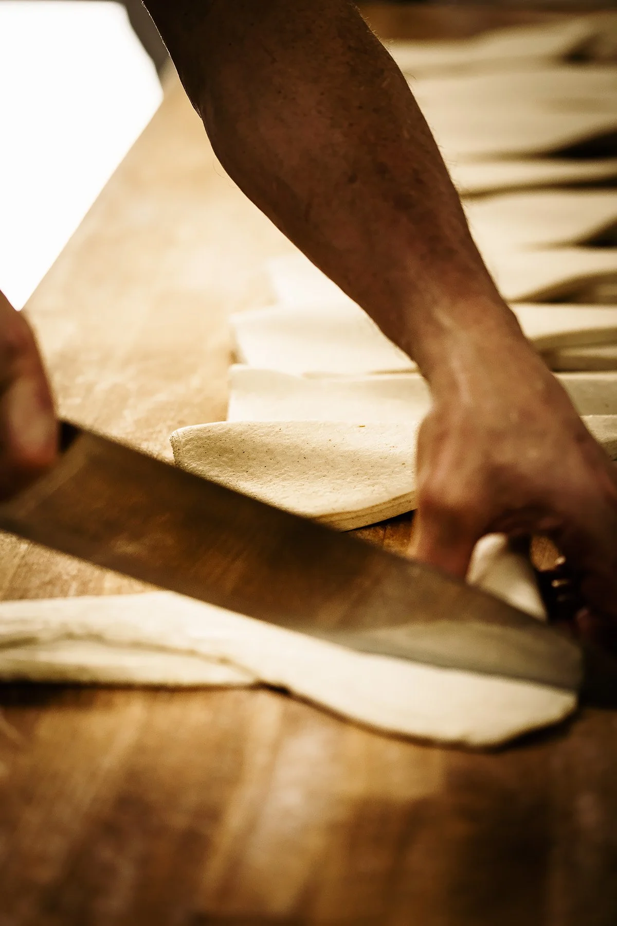 A person's hand slicing rolled dough with a knife on a wooden surface.
