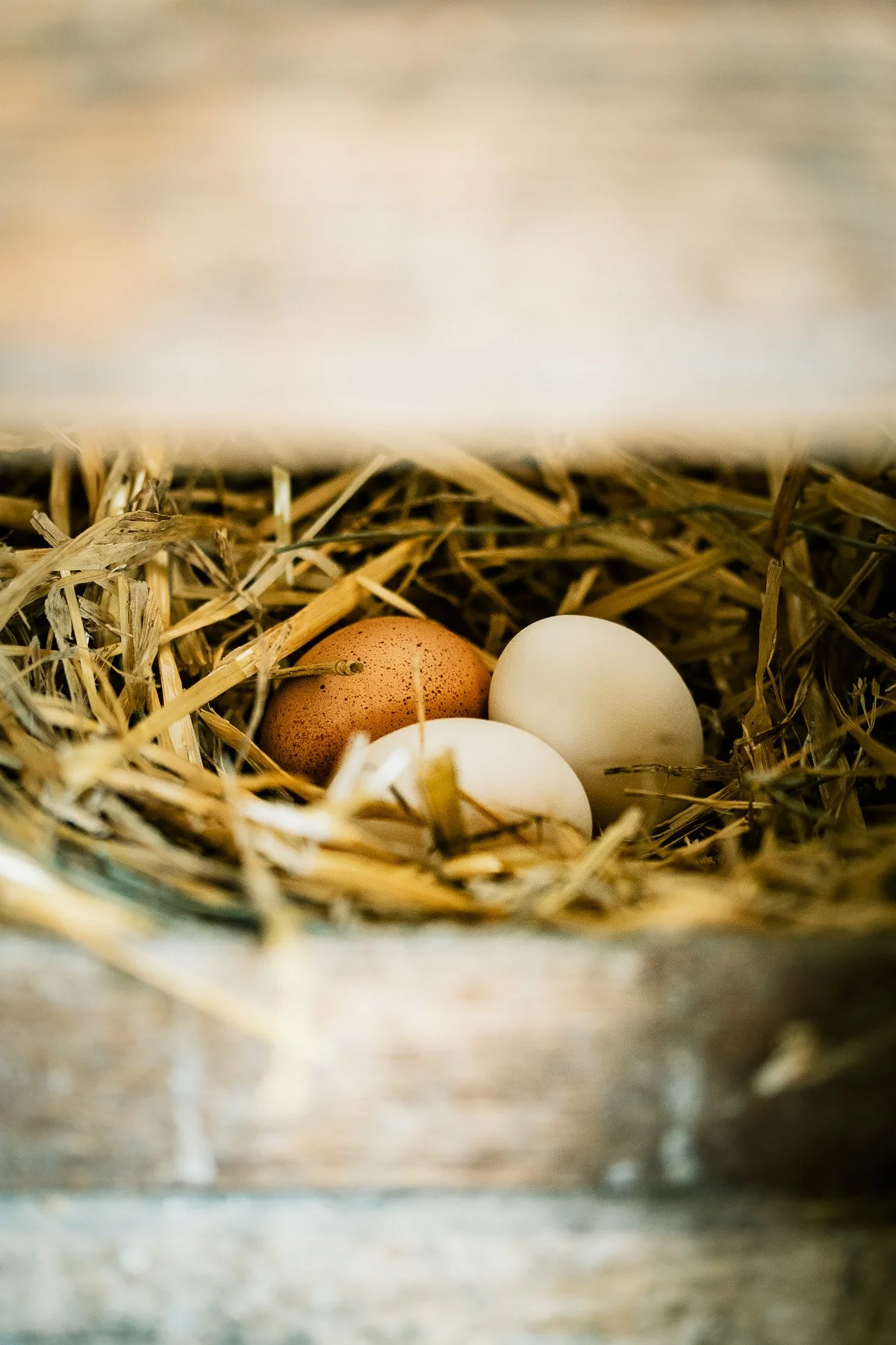 Three eggs in a nest made of straw in a wooden box.