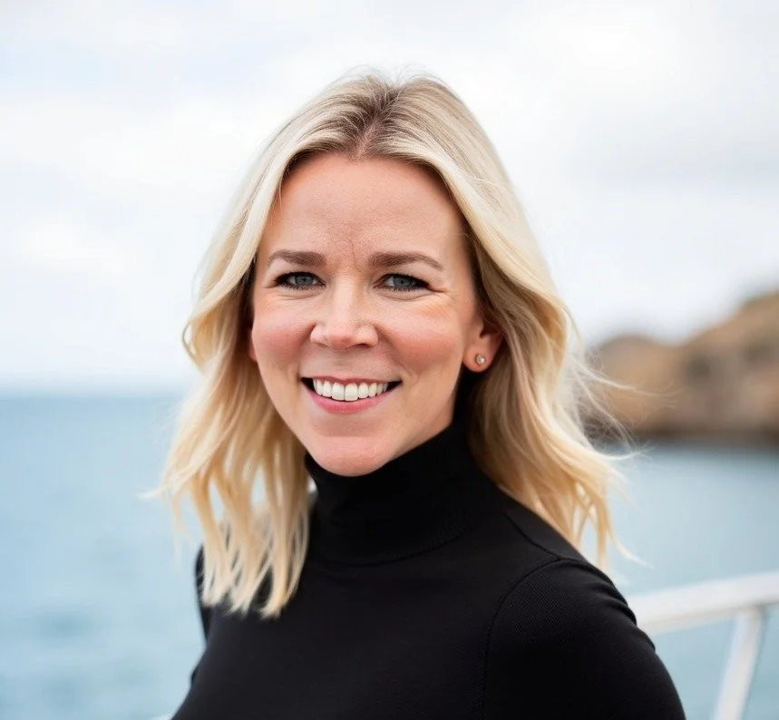 Smile of a blonde woman wearing a black turtleneck against a seascape background.