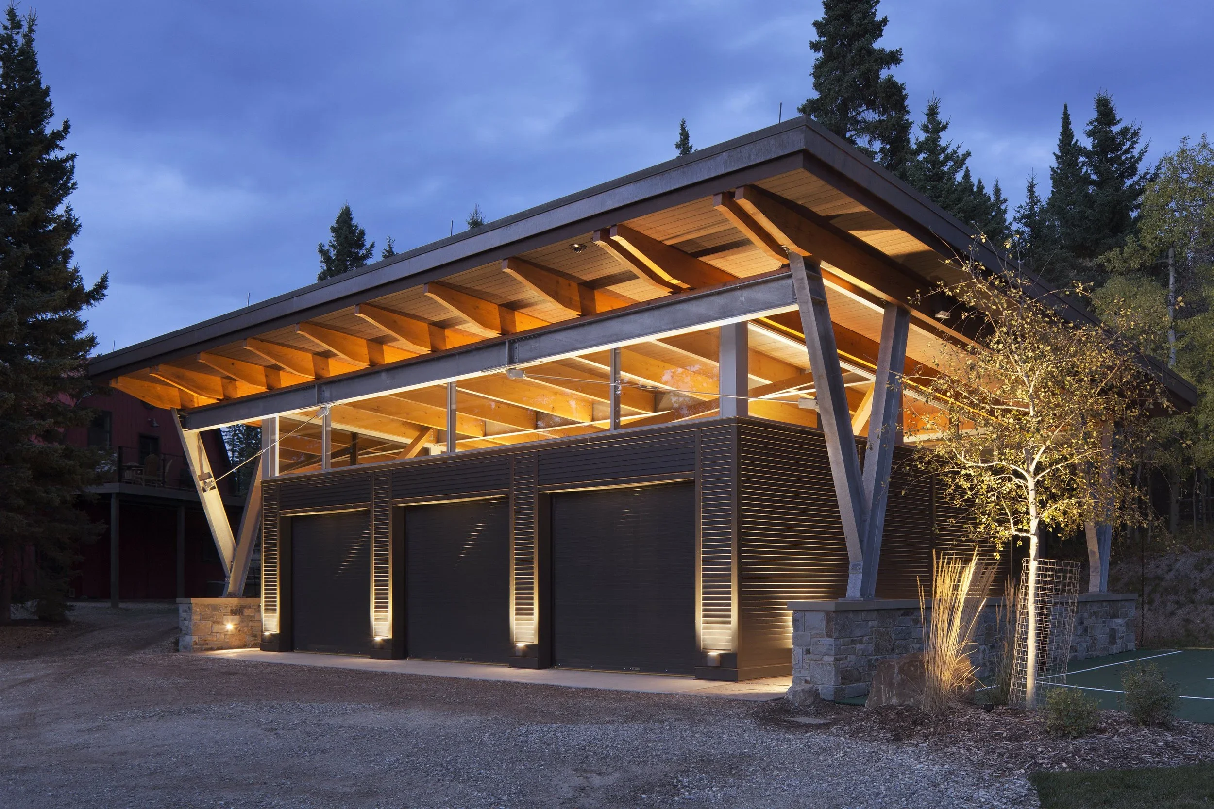 Modern building with a sloped roof, illuminated interior, and a small tree with lights at night. Dda Architecture Ltd.