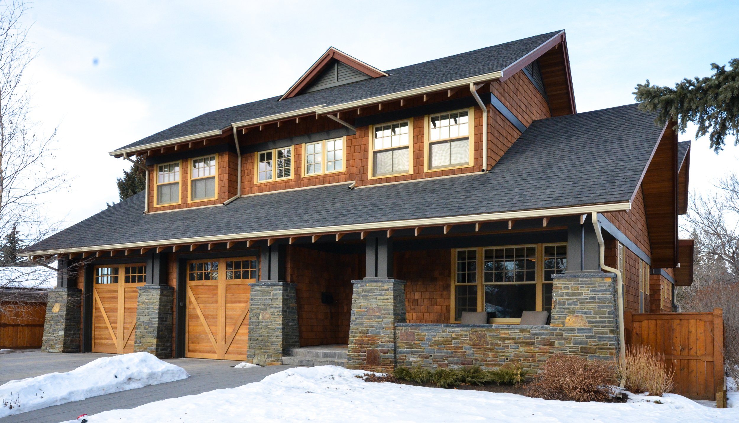 A large two-story house with a dark shingle roof, wooden siding, and stone accents, surrounded by snow in a residential neighborhood.