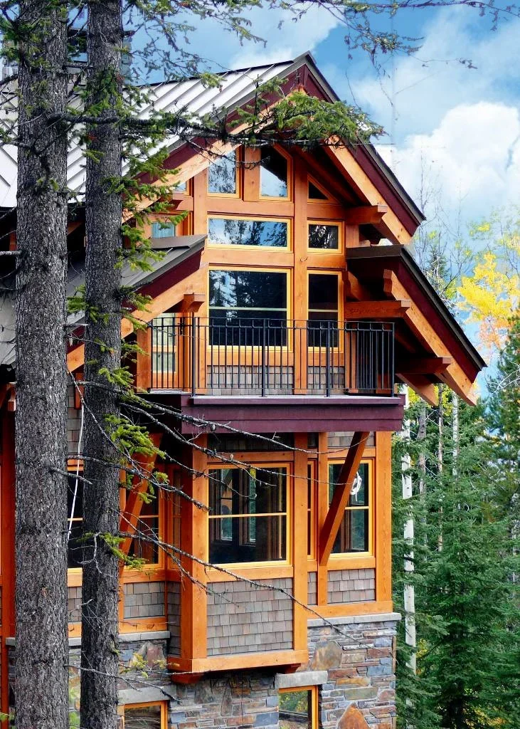 A multi-story wooden house with large windows, a balcony, surrounded by trees in a forested area. Dda Architecture Ltd.