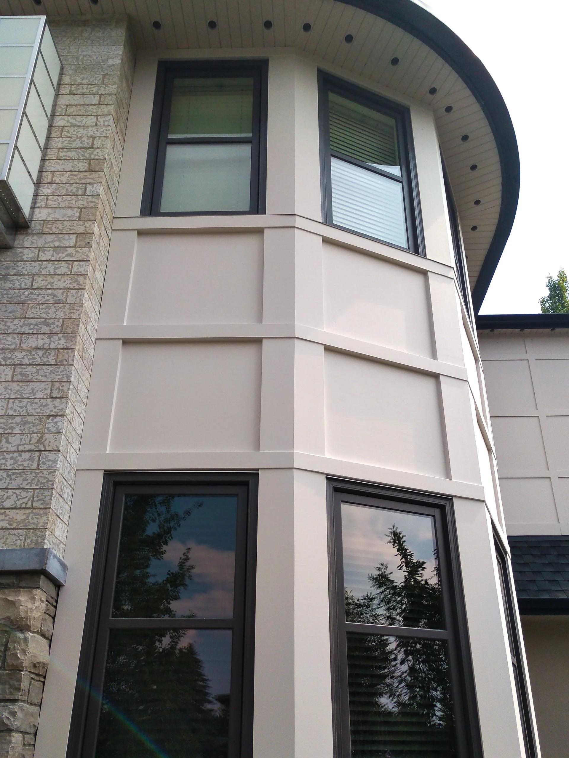Close-up view of a modern house corner with beige siding, black-framed windows, and a curved roof overhang.