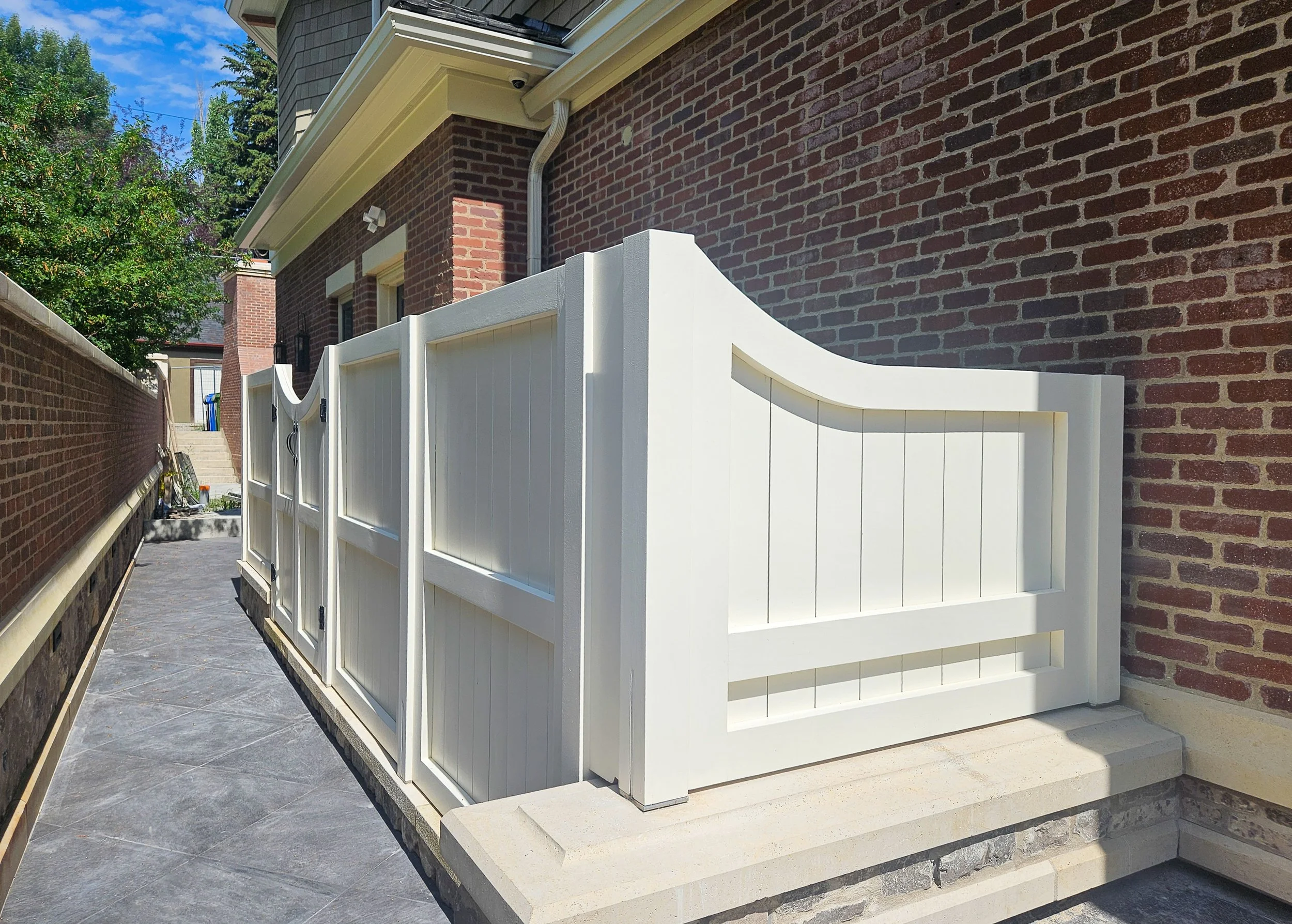 White privacy fence along side of a brick house, with steps and paved walkway.