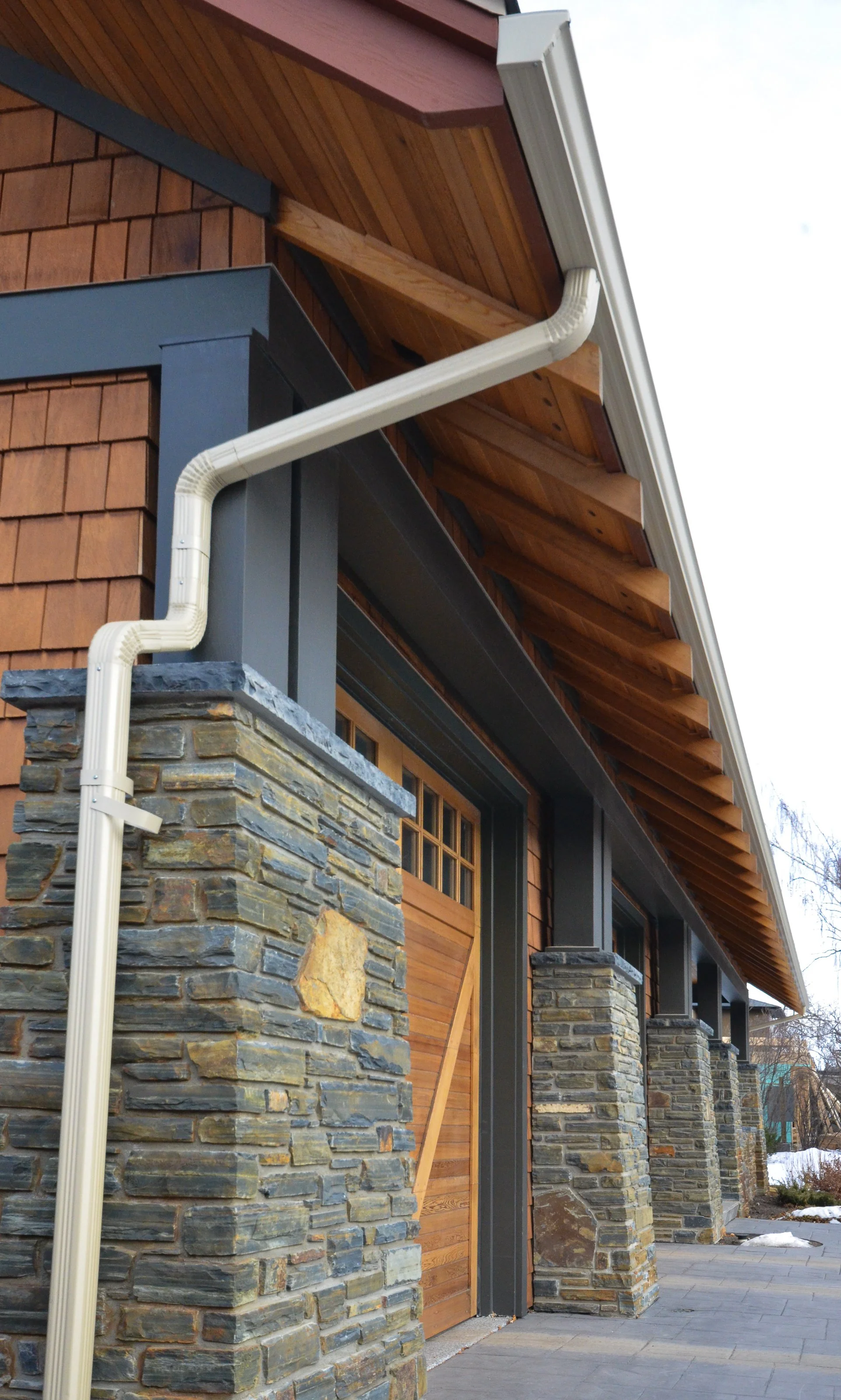 Close-up of a house's exterior showing stone columns, wood siding, and a metal gutter system.