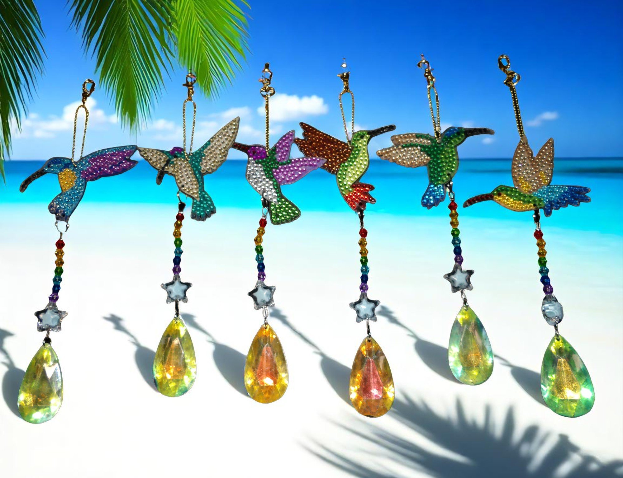 Colorful hummingbird keychains hanging with a tropical beach and palm tree in the background.