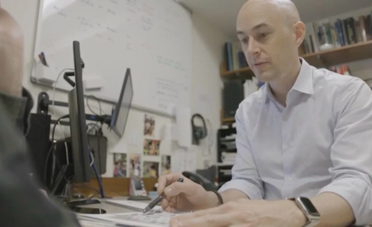 Christopher Benjamin PhD, a neuropsychologist in Vancouver BC, sitting at a desk and testing a patient in his office.