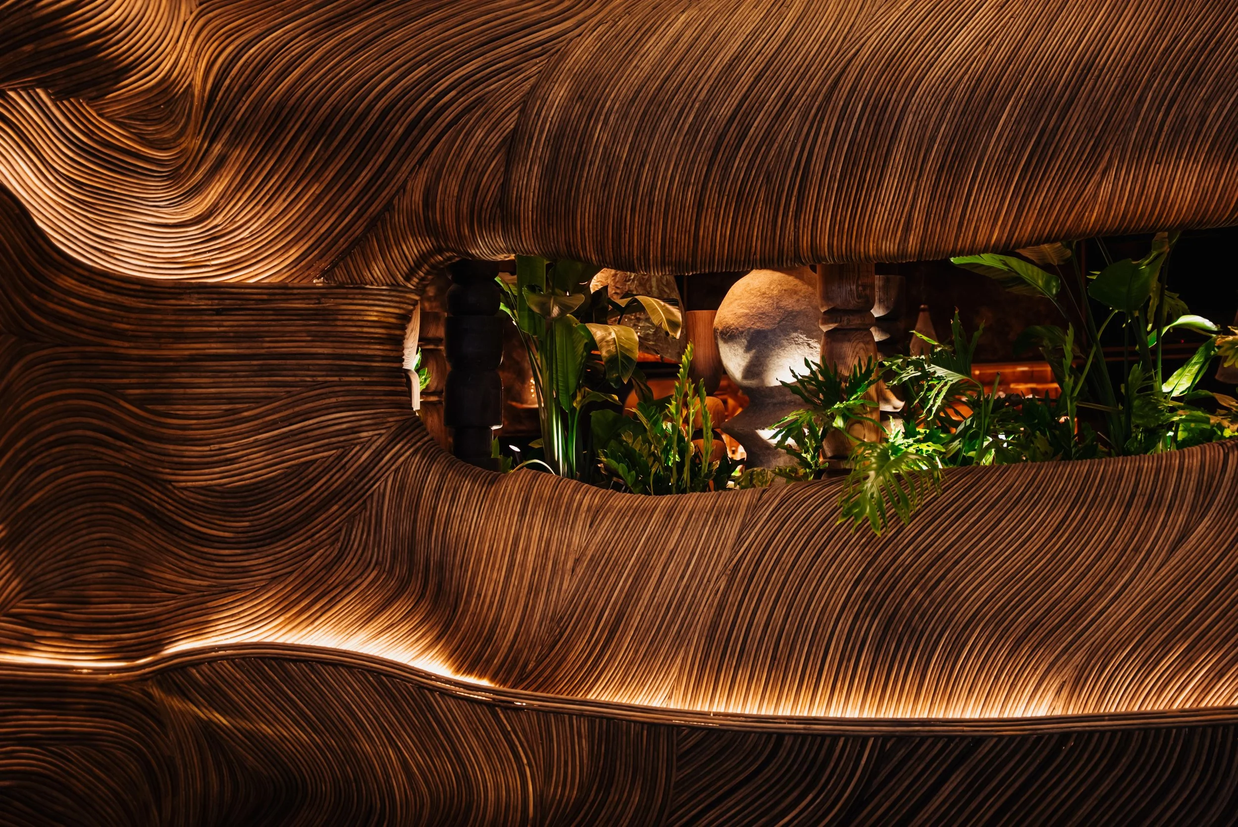 Amaya Modern Mexican interior at The Cosmopolitan of Las Vegas, featuring warm earthen finishes, curved banquettes, woven wall details, lush greenery, and softly illuminated sculptural forms.