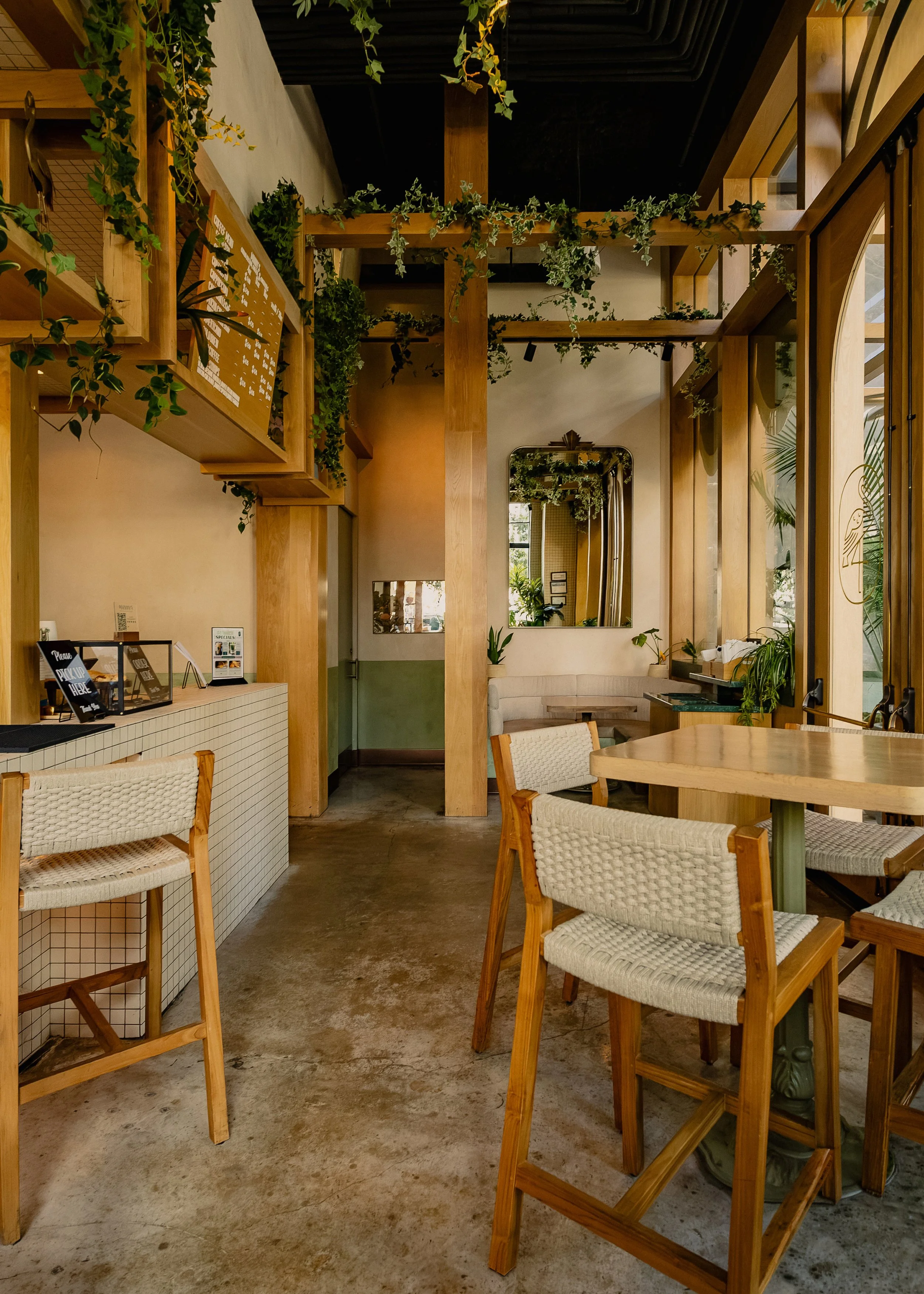 Light-filled interior at Manny’s featuring white tile, natural wood details, open shelving and abundant greenery.