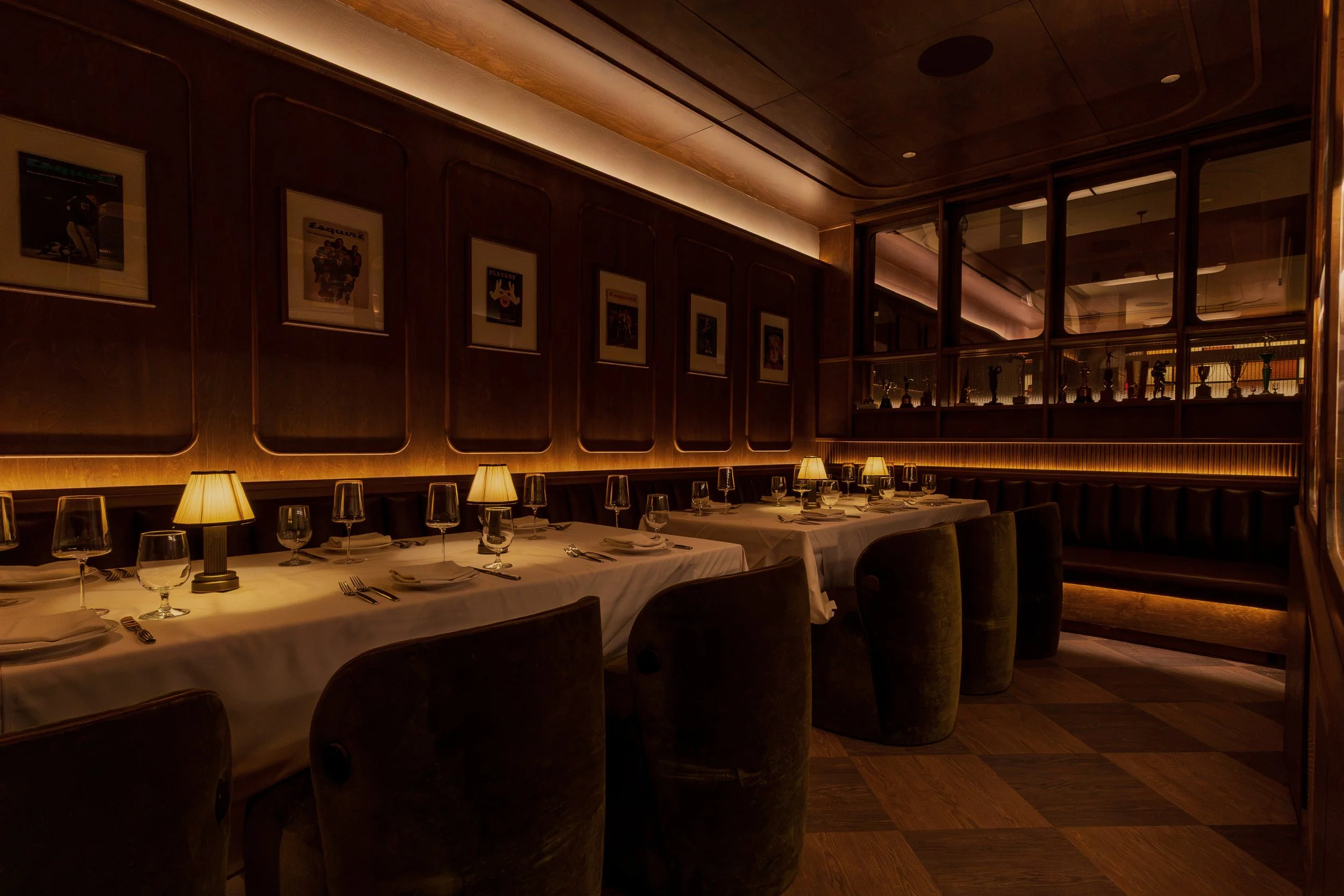 A long communal table is lined with upholstered chairs beneath a gallery wall of framed sports photographs and warm integrated lighting.