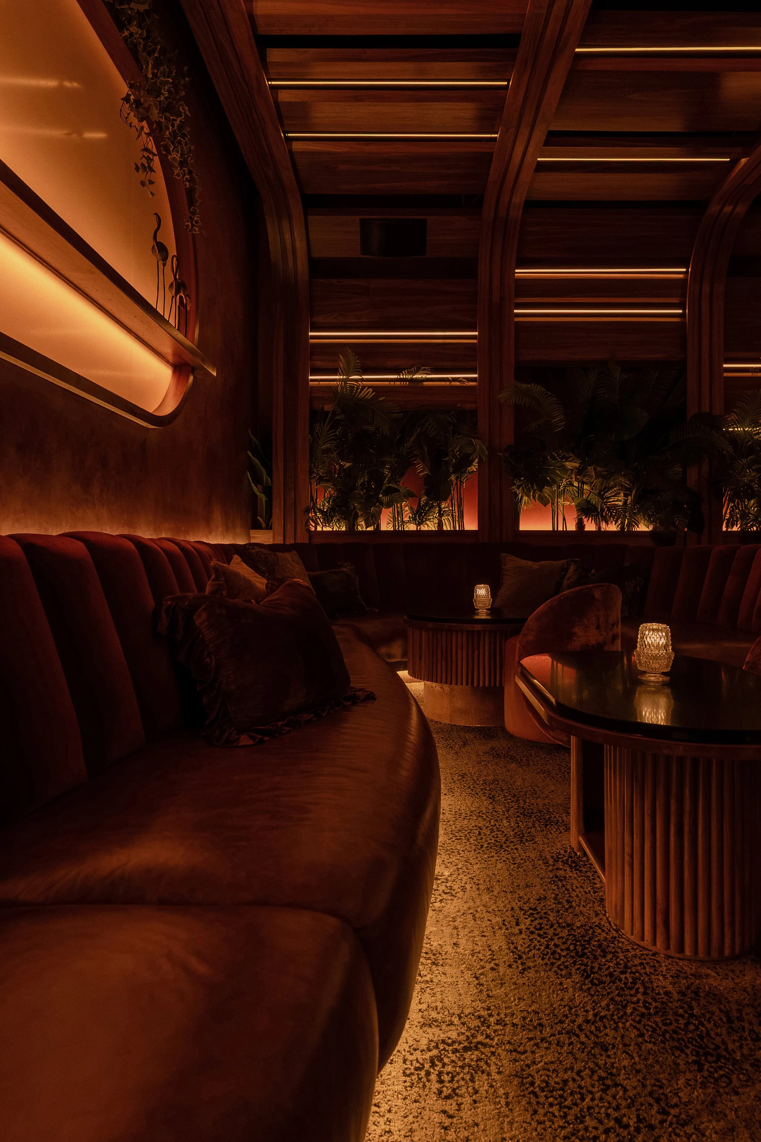 Close view of Powder Room’s curved upholstered banquette with patterned carpet, wood tables and amber architectural lighting.