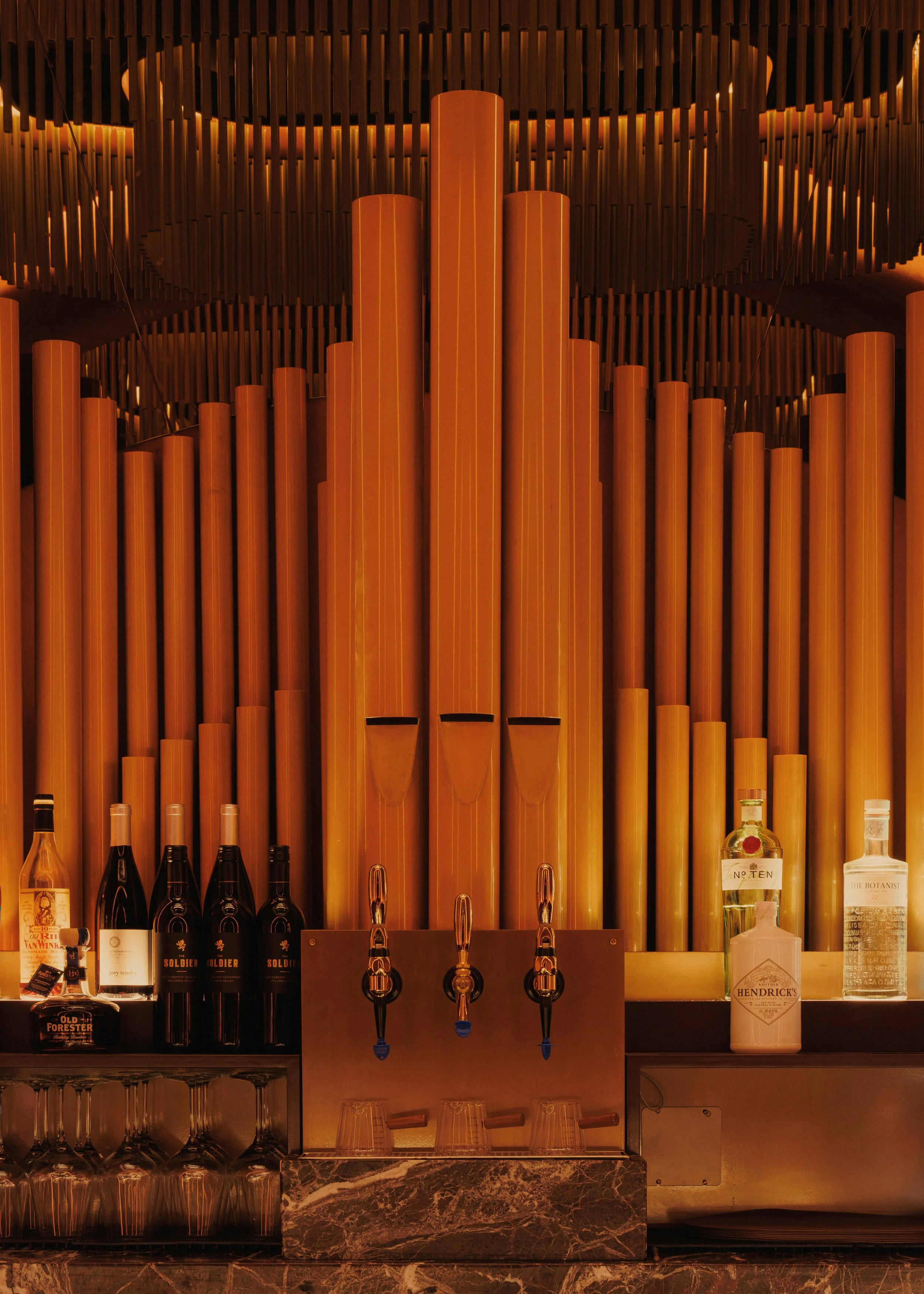 Close-up of Mea Culpa’s organ-inspired bar installation, with illuminated pipes, dark metal fins, marble detailing and integrated beverage taps.