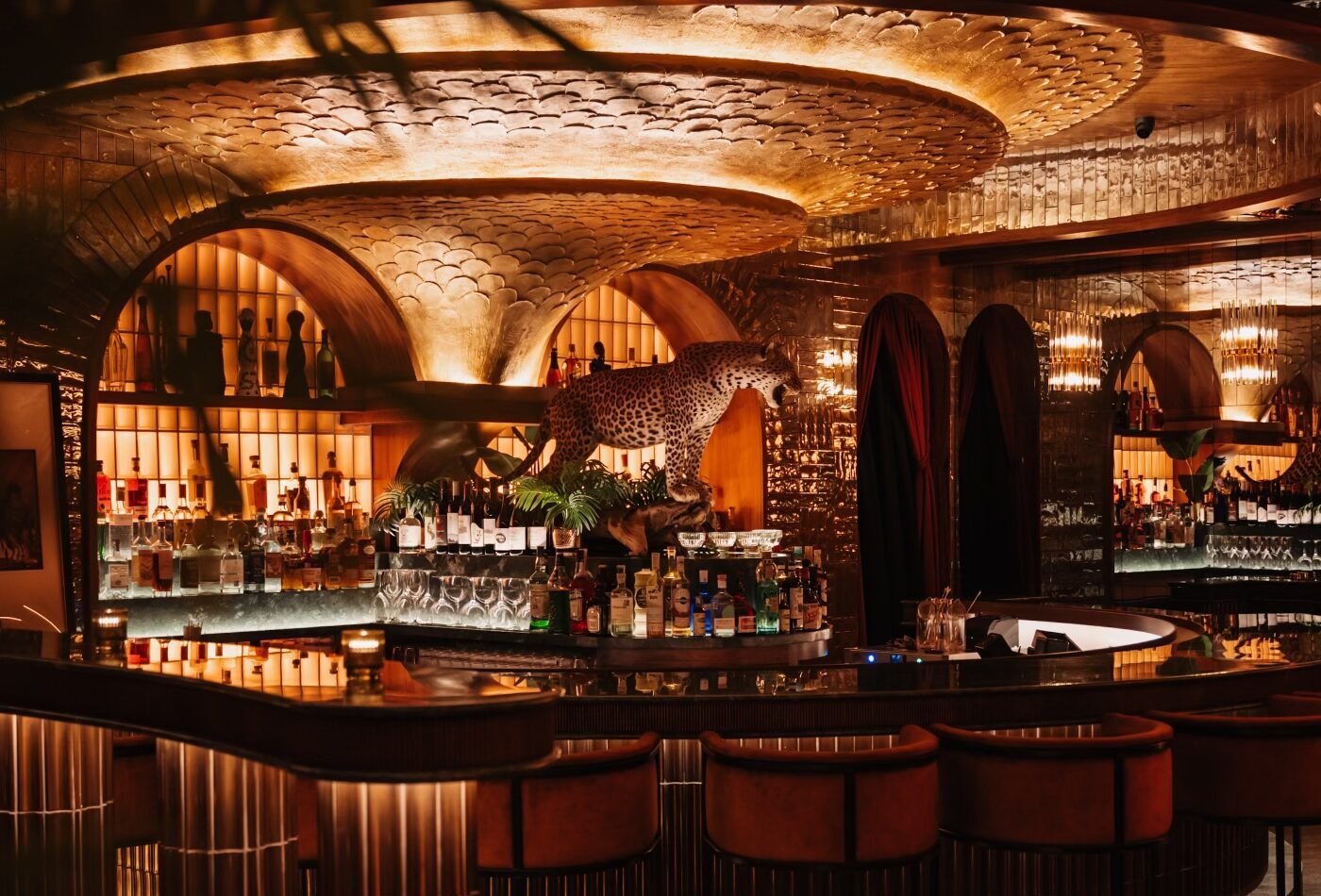 Powder Room cocktail lounge in downtown Austin featuring a sculptural gold ceiling, illuminated arched back bar and leopard display designed by PETERMAX Co.