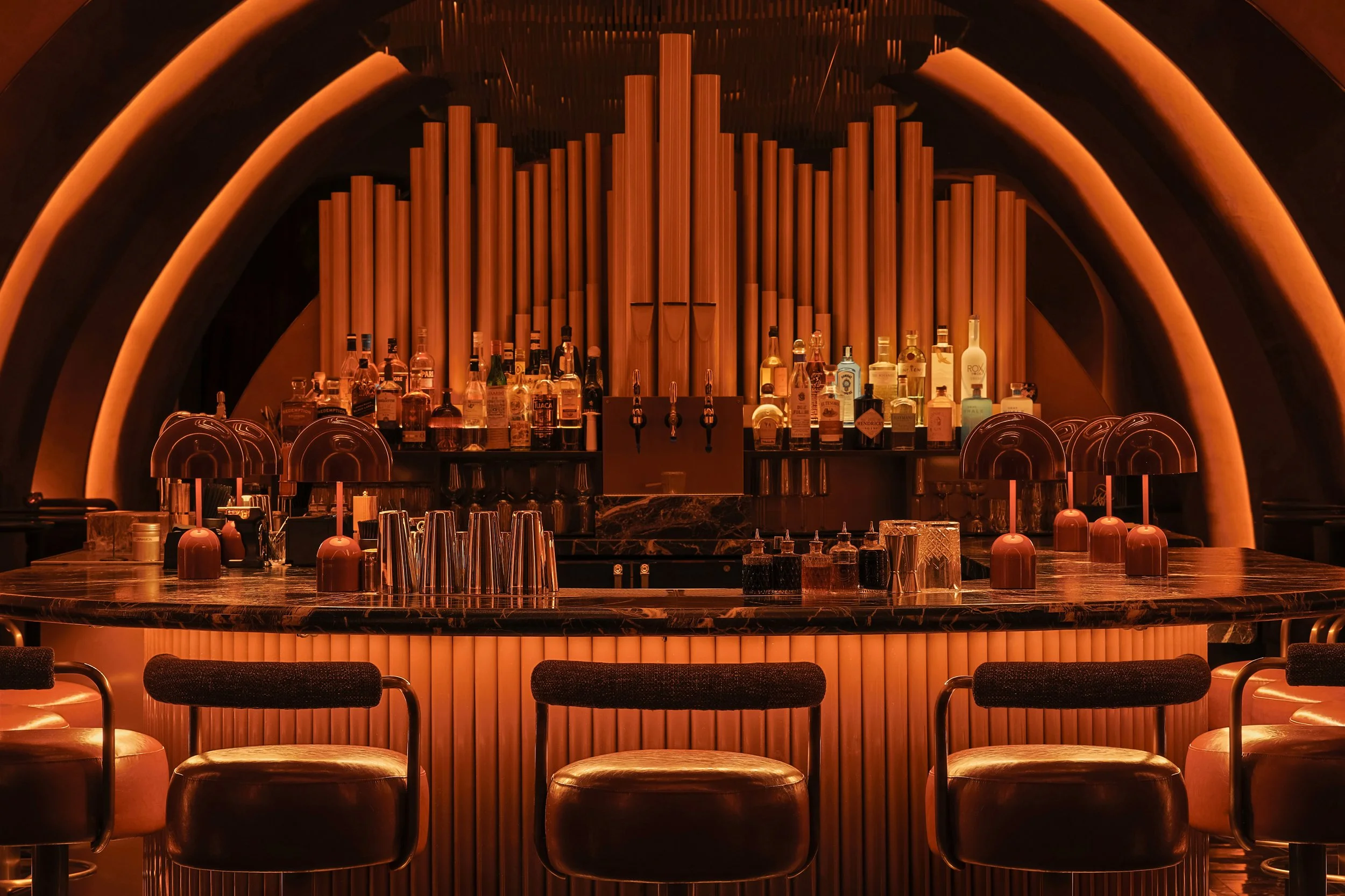 Close view of Mea Culpa’s bar with leather stools, fluted illuminated millwork and a dramatic pipe-organ installation.