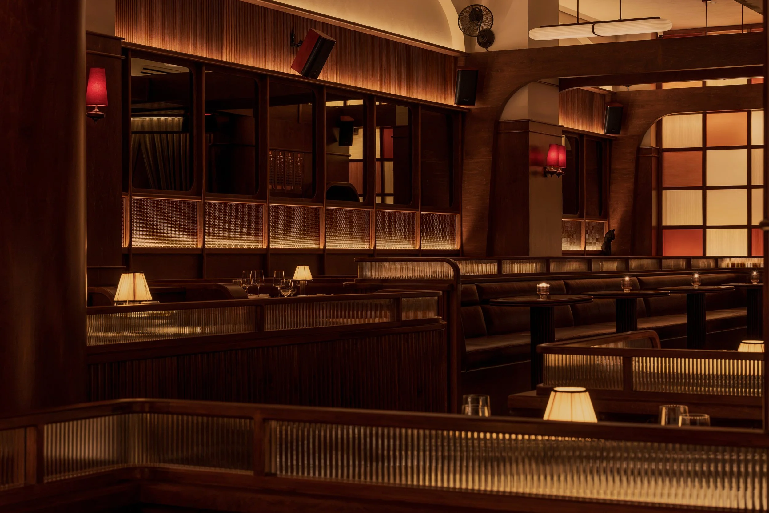 Intimate leather booths sit beneath decorative metal screens and interior windows that connect the club’s layered spaces.
