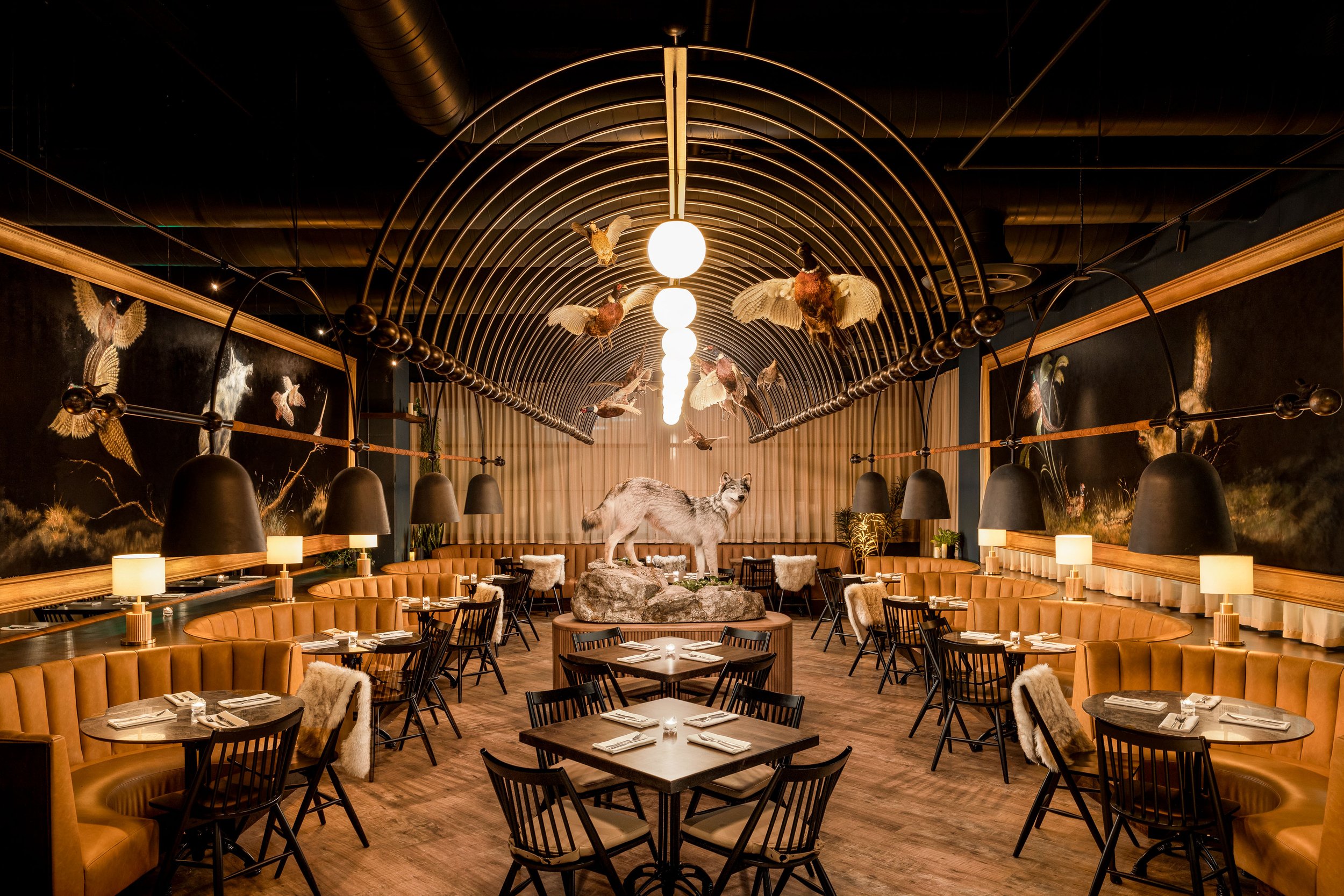 Wren & Wolf restaurant interior in Phoenix with warm lighting, wood details, banquette seating, and sculptural circular ceiling fixtures.