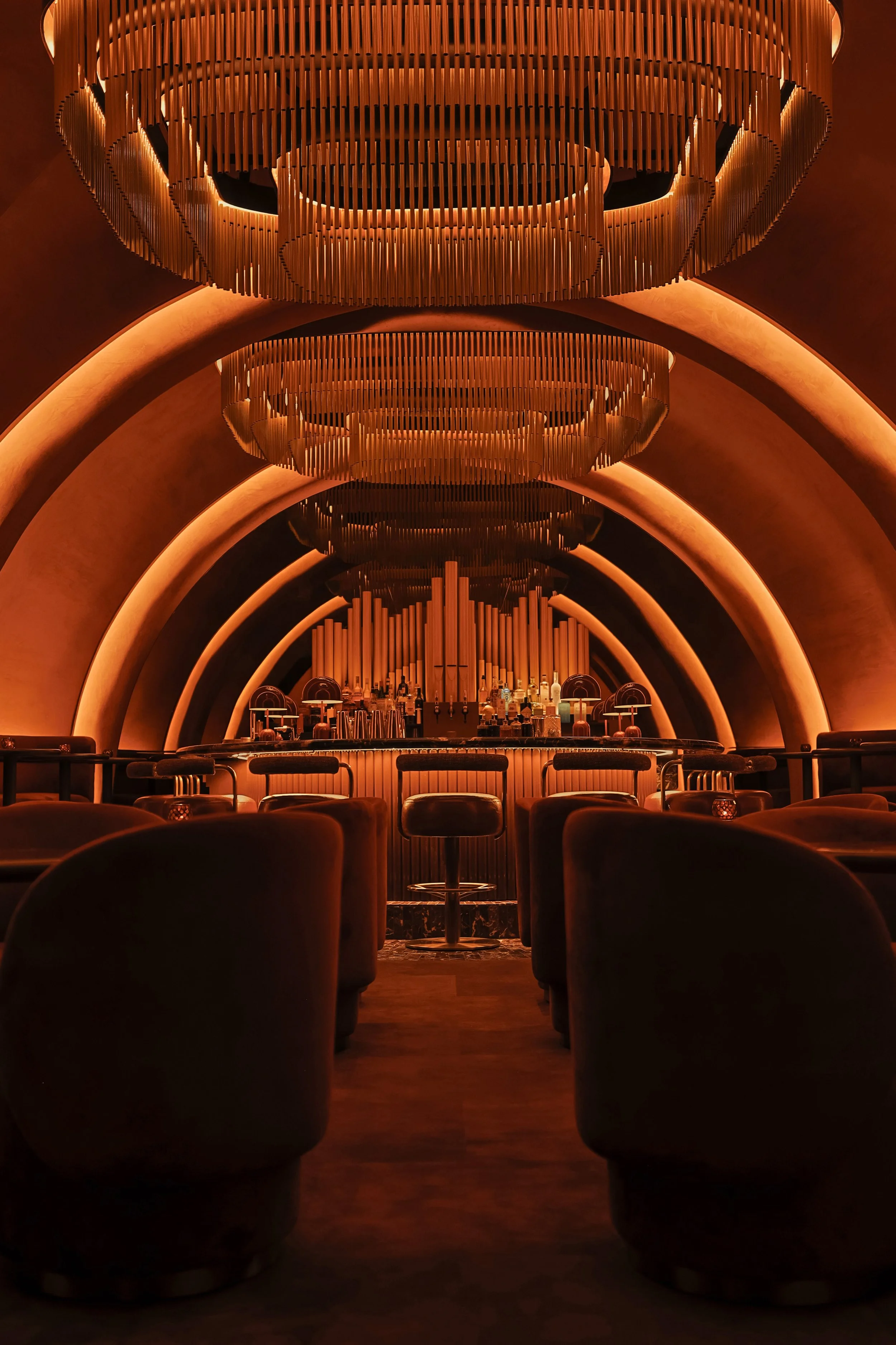 Layered metal chandeliers align beneath Mea Culpa’s glowing arches, drawing the eye toward the organ-inspired bar at the end of the lounge.