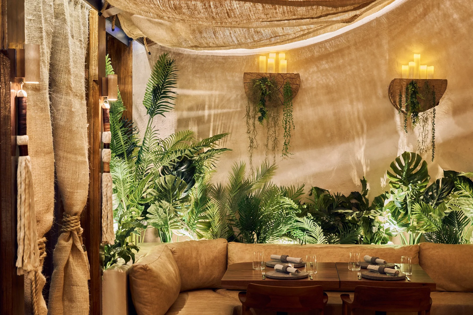 tán New York restaurant interior in Midtown Manhattan, featuring lush tropical greenery, warm plaster walls, woven materials, leather banquette seating, and soft candlelight.