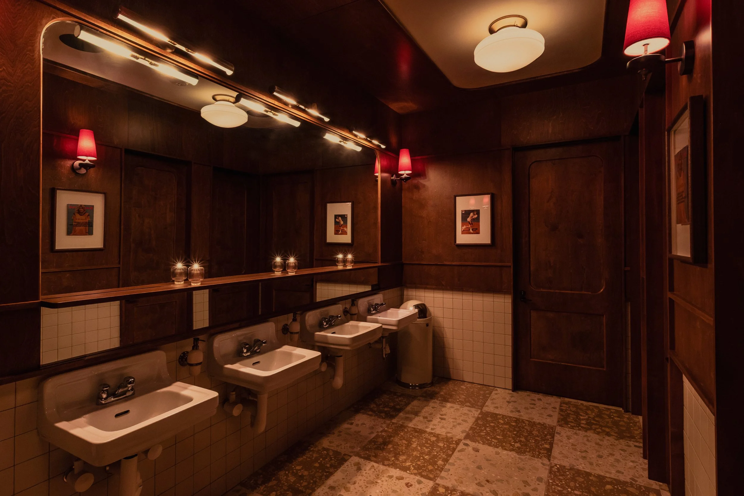 Austin Sports Club’s restroom features marble basins, dark wood partitions, patterned flooring and vintage-inspired lighting.