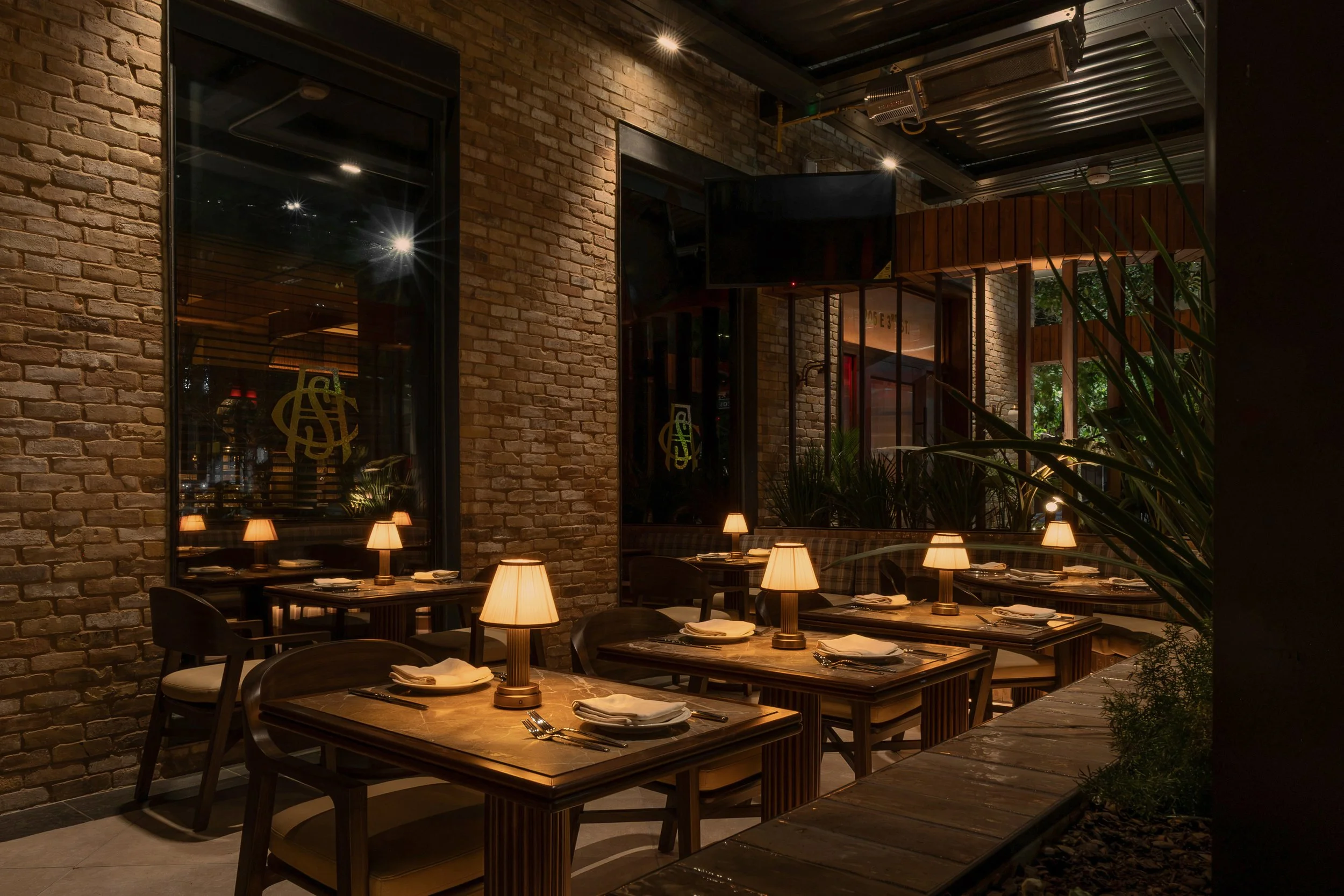 Intimate dining tables sit among exposed brick, black-framed windows and climbing greenery at Austin Sports Club.