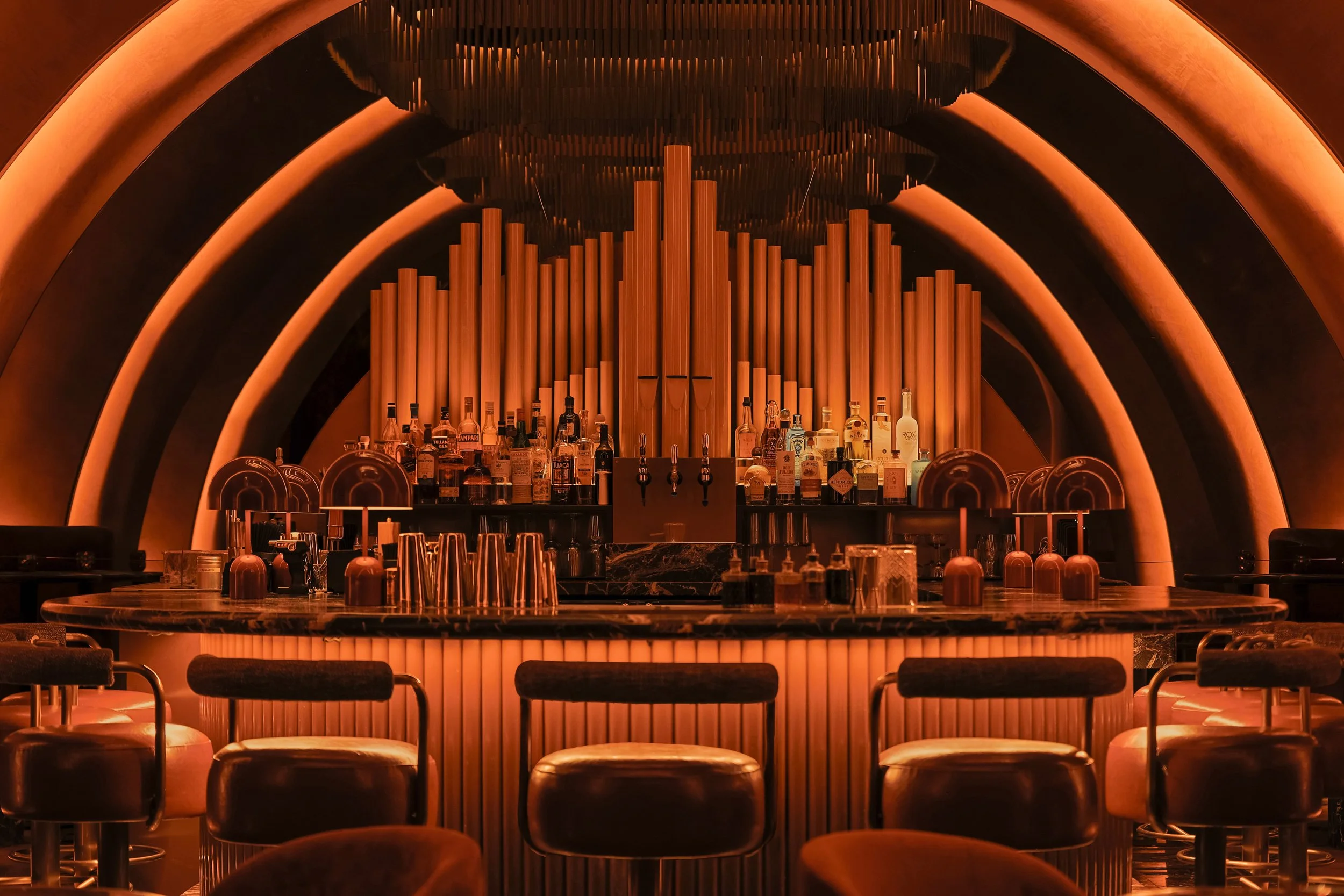 Direct view of Mea Culpa’s marble bar and illuminated fluted base, backed by a dramatic sculptural arrangement of organ pipes.