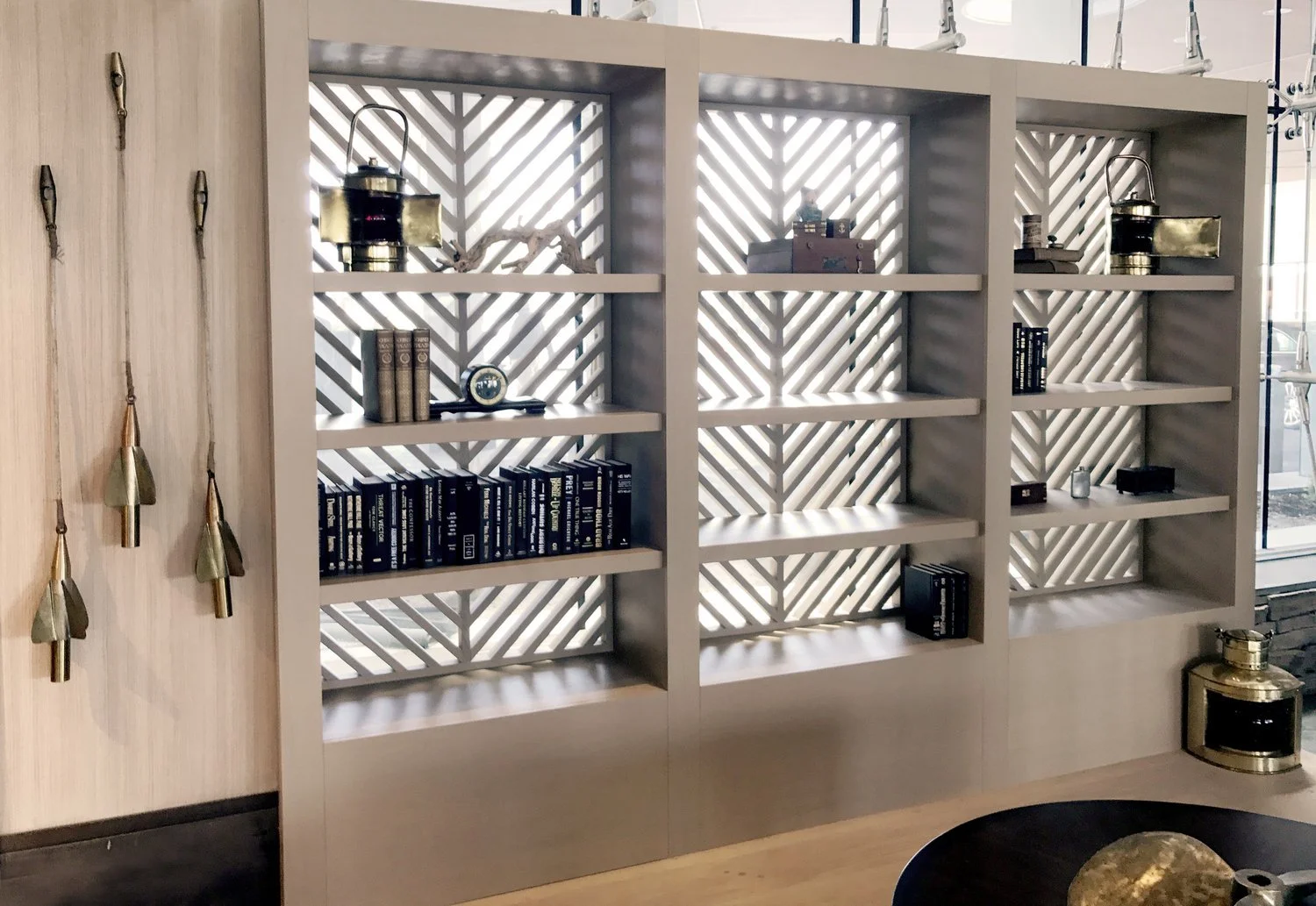 Modern white bookshelf with decorative objects and books, set against a background with geometric patterns, and adjacent wall with metallic hanging ornaments.