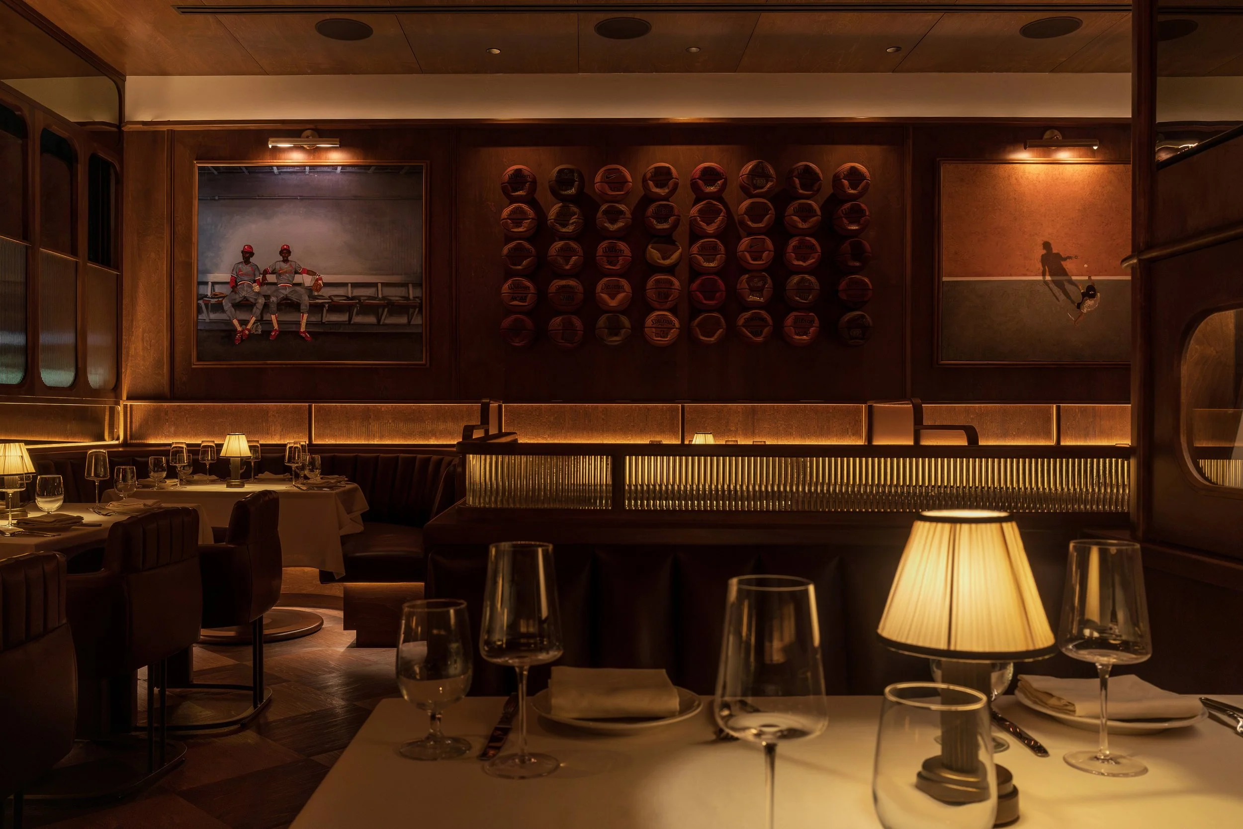 A grid of vintage basketballs creates a striking feature wall above leather banquettes and candlelit dining tables.