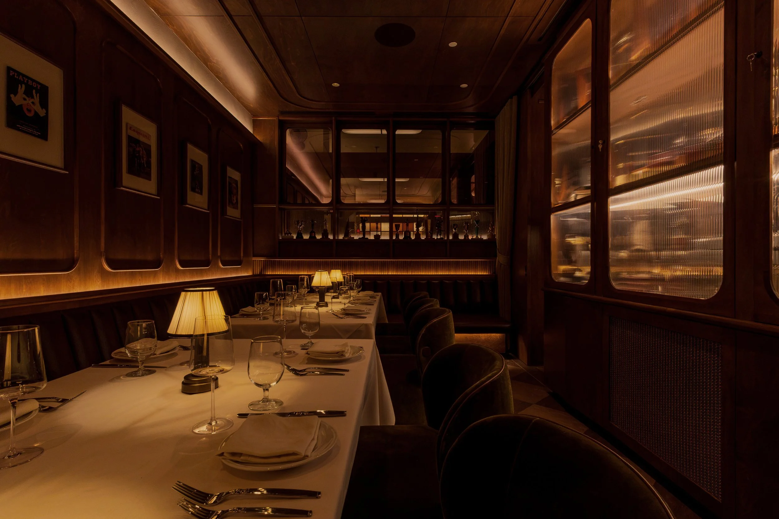 A long dining table in PDR is set beneath warm lighting beside custom display cabinets filled with vintage sports memorabilia.