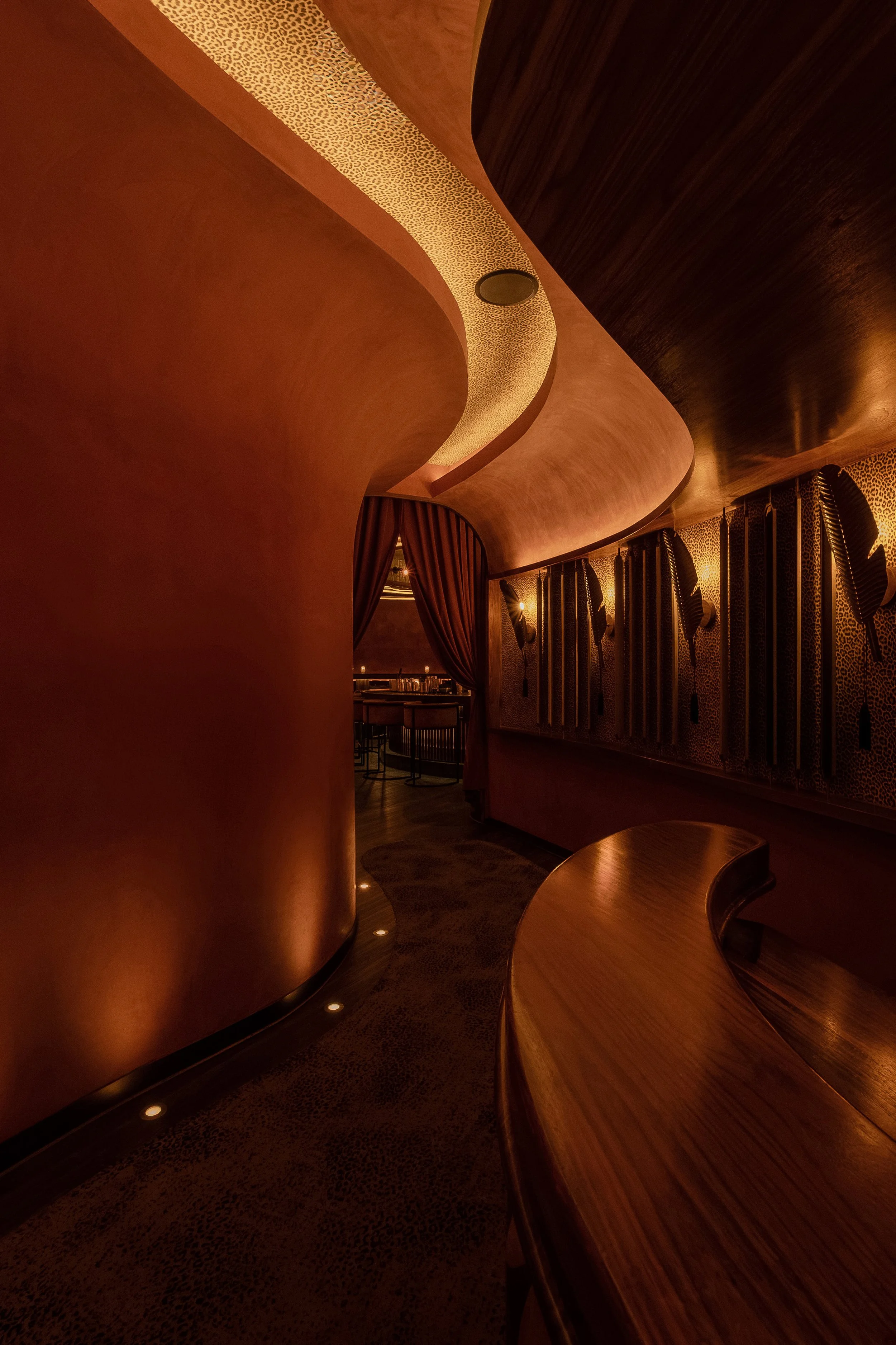 Curved corridor at Powder Room in Austin featuring a sculptural illuminated ceiling, textured wall panels, custom wood millwork and patterned flooring.