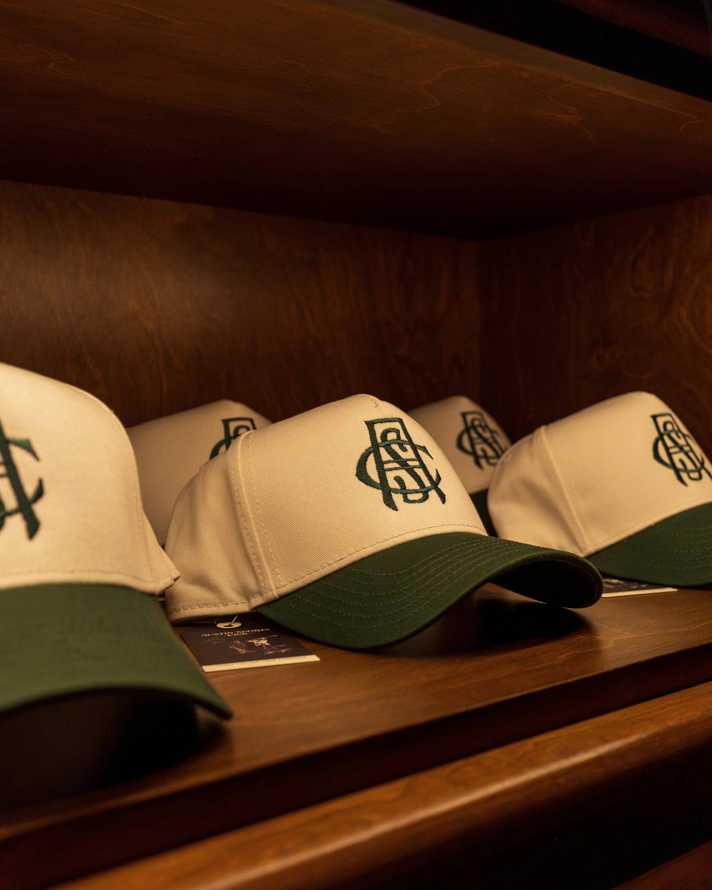 Branded Austin Sports Club caps displayed on a custom wood shelf.