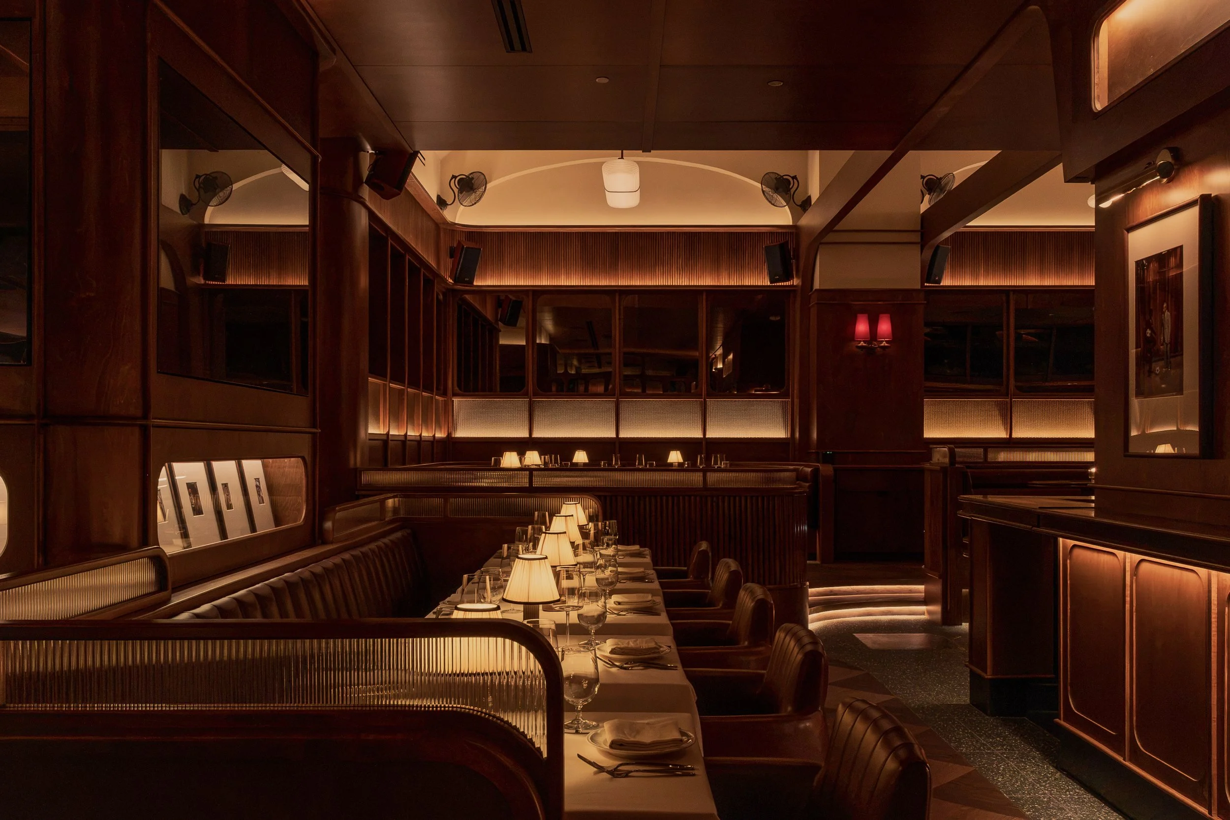 A long dining table extends toward illuminated display cabinets, surrounded by leather seating and warm wood finishes.