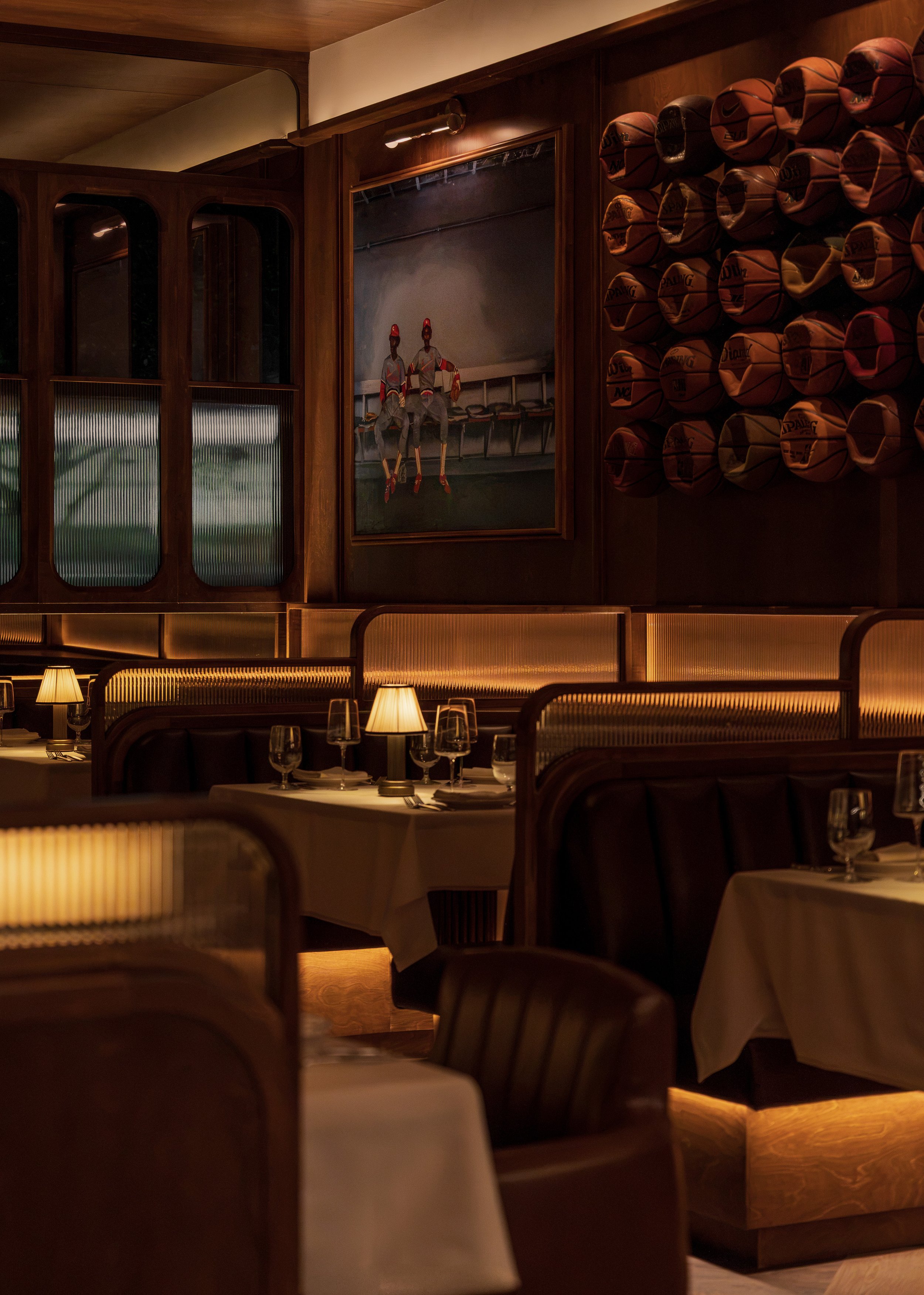 Layered sports displays and vintage basketballs provide the backdrop for curved booths and softly illuminated dining tables.