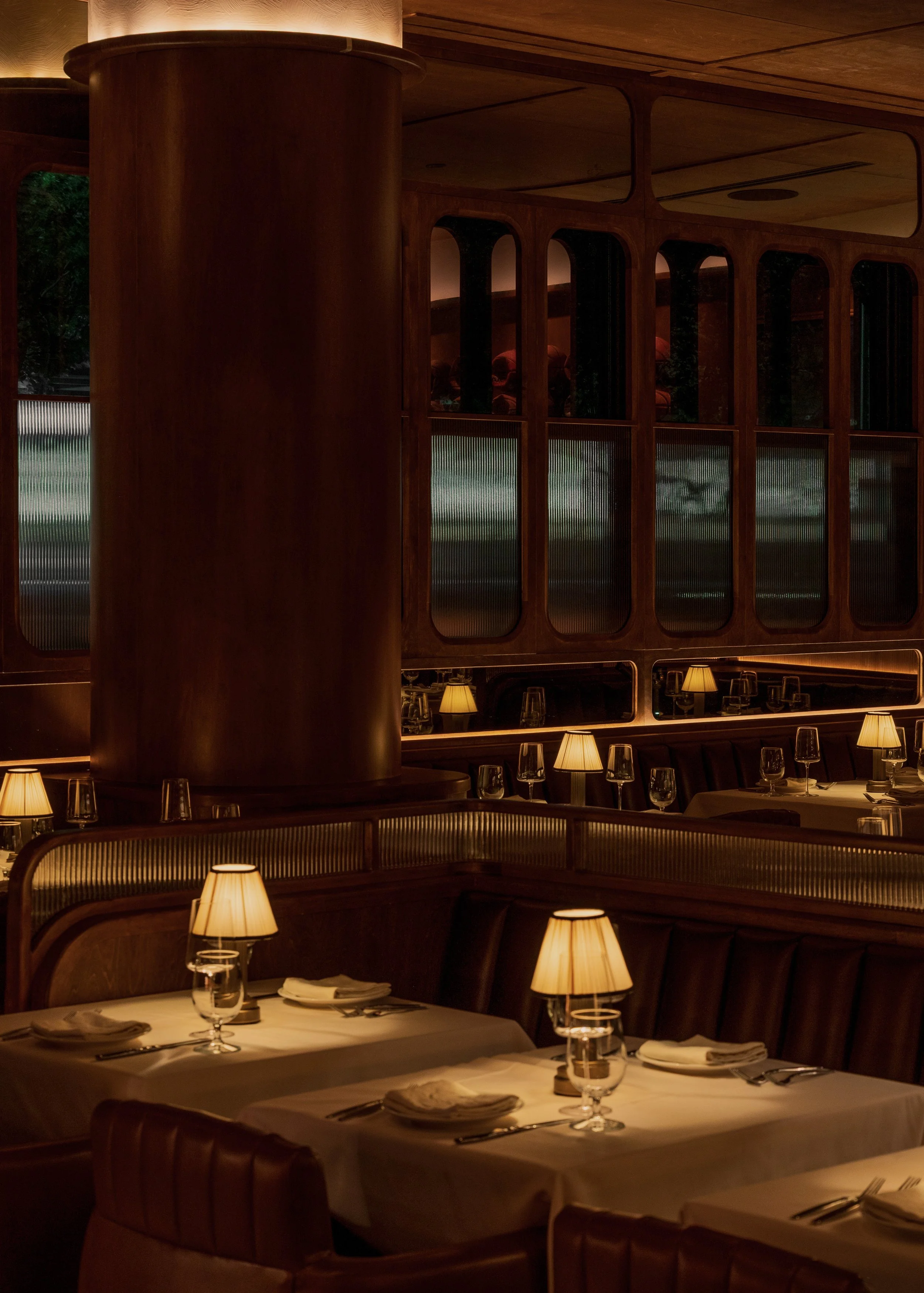 Arched glass display cabinets, dark wood paneling and shaded table lamps frame an intimate dining area.