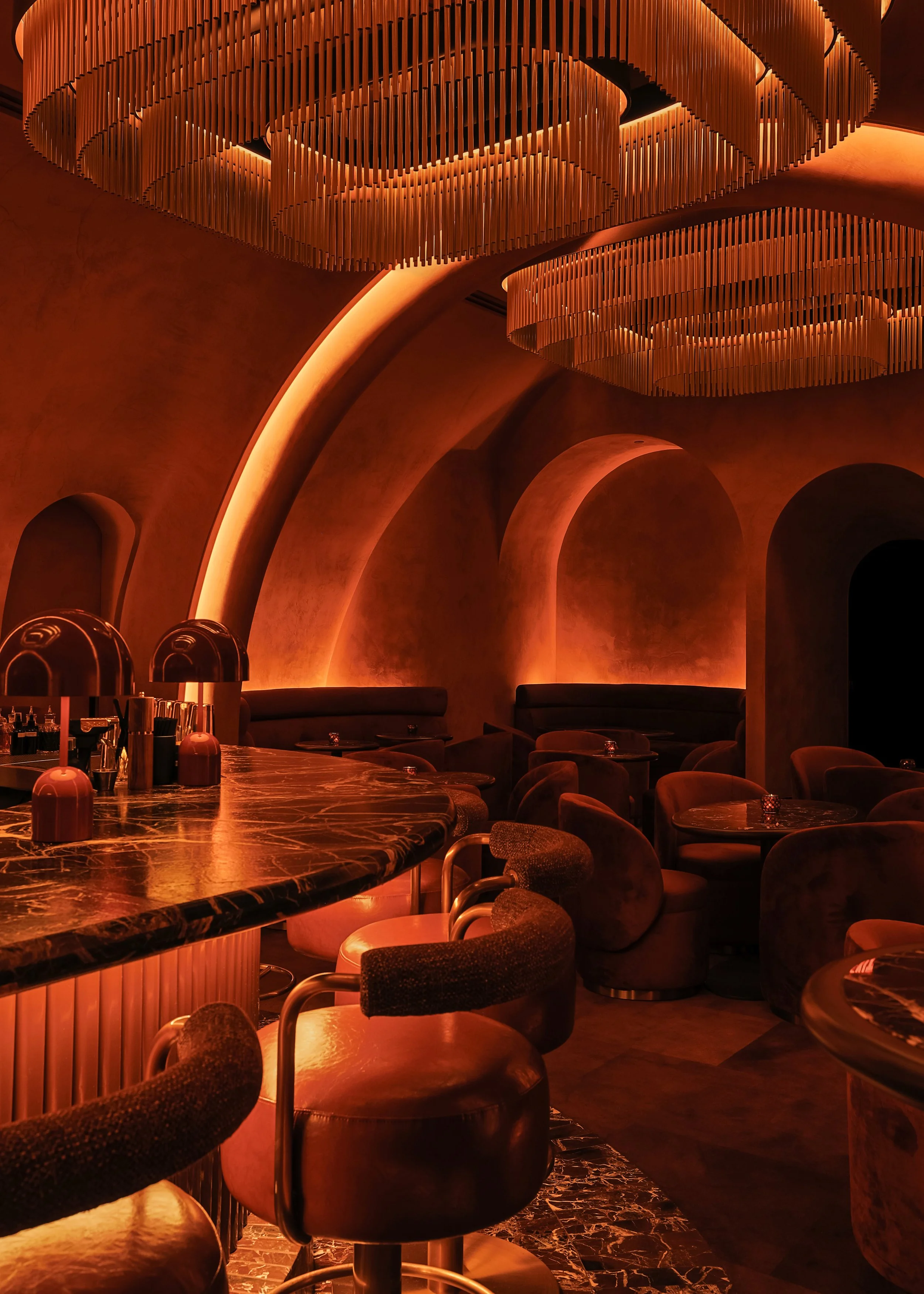 Intimate cocktail seating beneath Mea Culpa’s illuminated arches, with velvet lounge chairs, candlelit tables and a view toward the central bar.