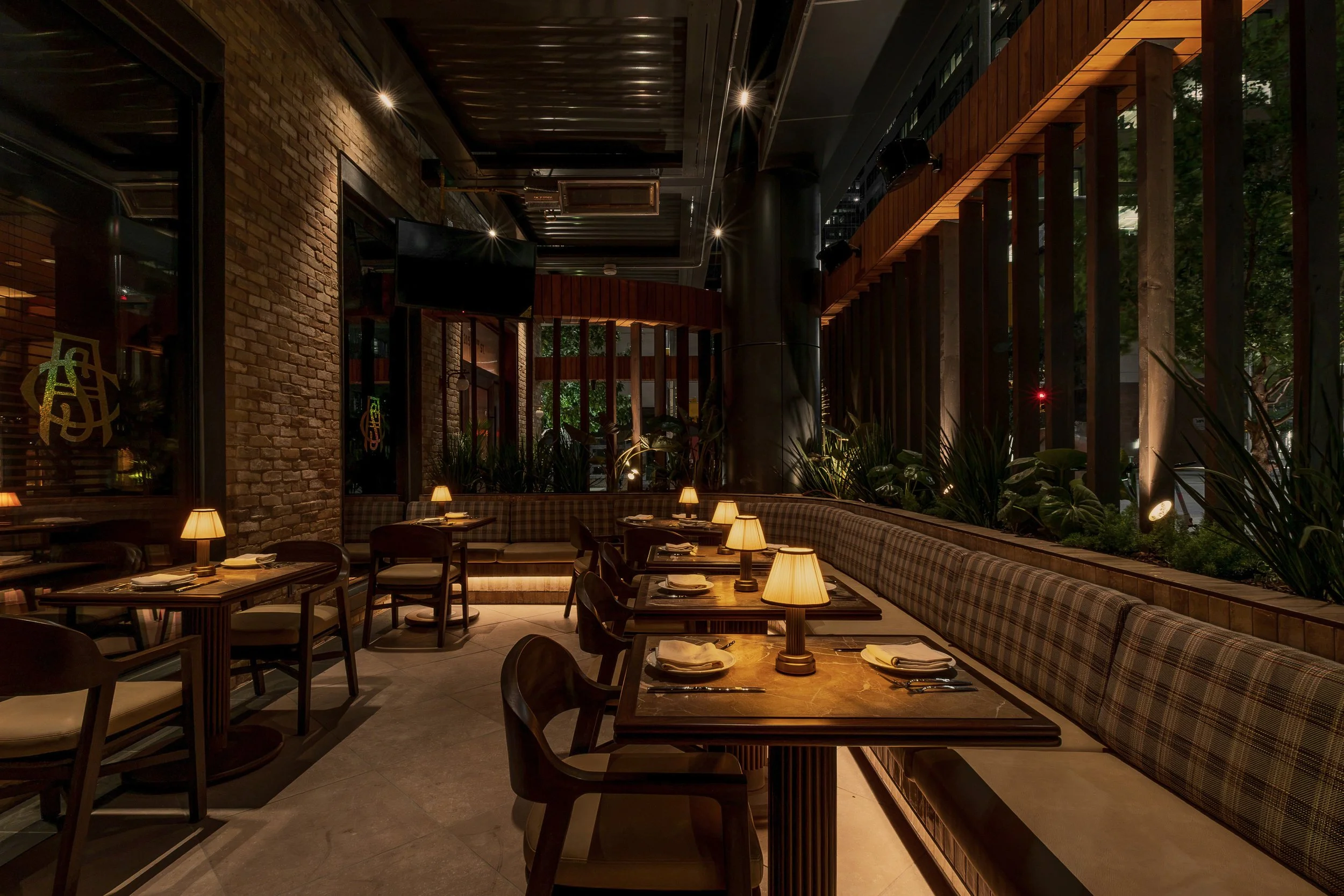 A garden-inspired dining room pairs exposed brick, dark metal framing and abundant greenery with candlelit tables.