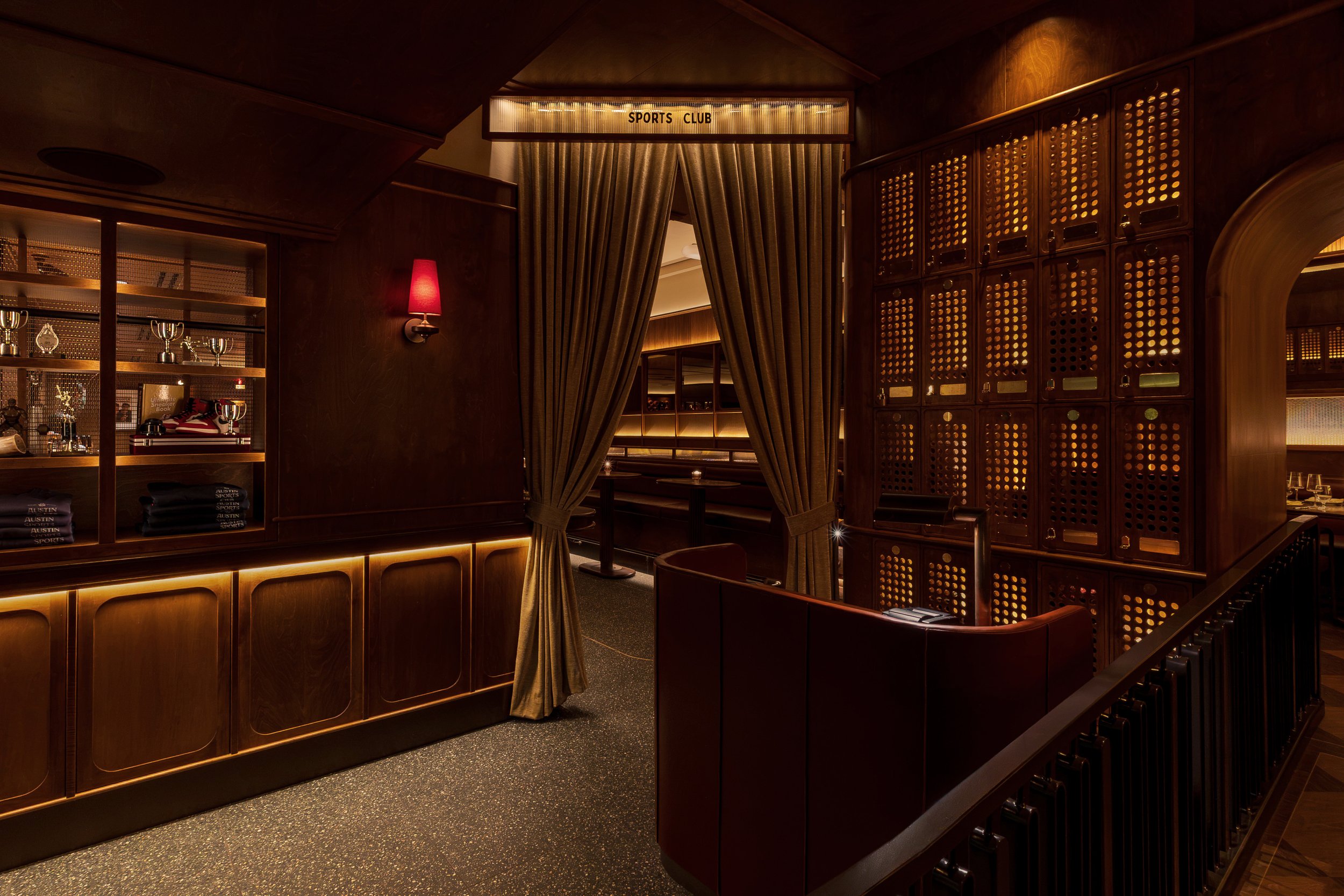 A softly illuminated staircase framed by bronze-toned metalwork rises beside an intimate leather banquette.