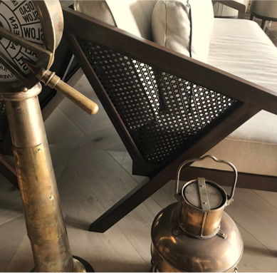 Close-up of a vintage brass and steel fire extinguisher and a brass lantern in a living room with a wooden side table and beige sofa.