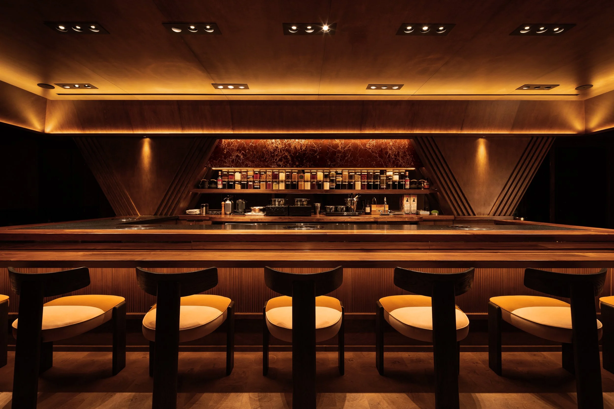 Uppercut’s 16-seat chef’s counter in downtown Phoenix, designed by PETERMAX Co. with rich wood surfaces, warm amber lighting, inset tabletop grills and illuminated dry-aging cabinets.