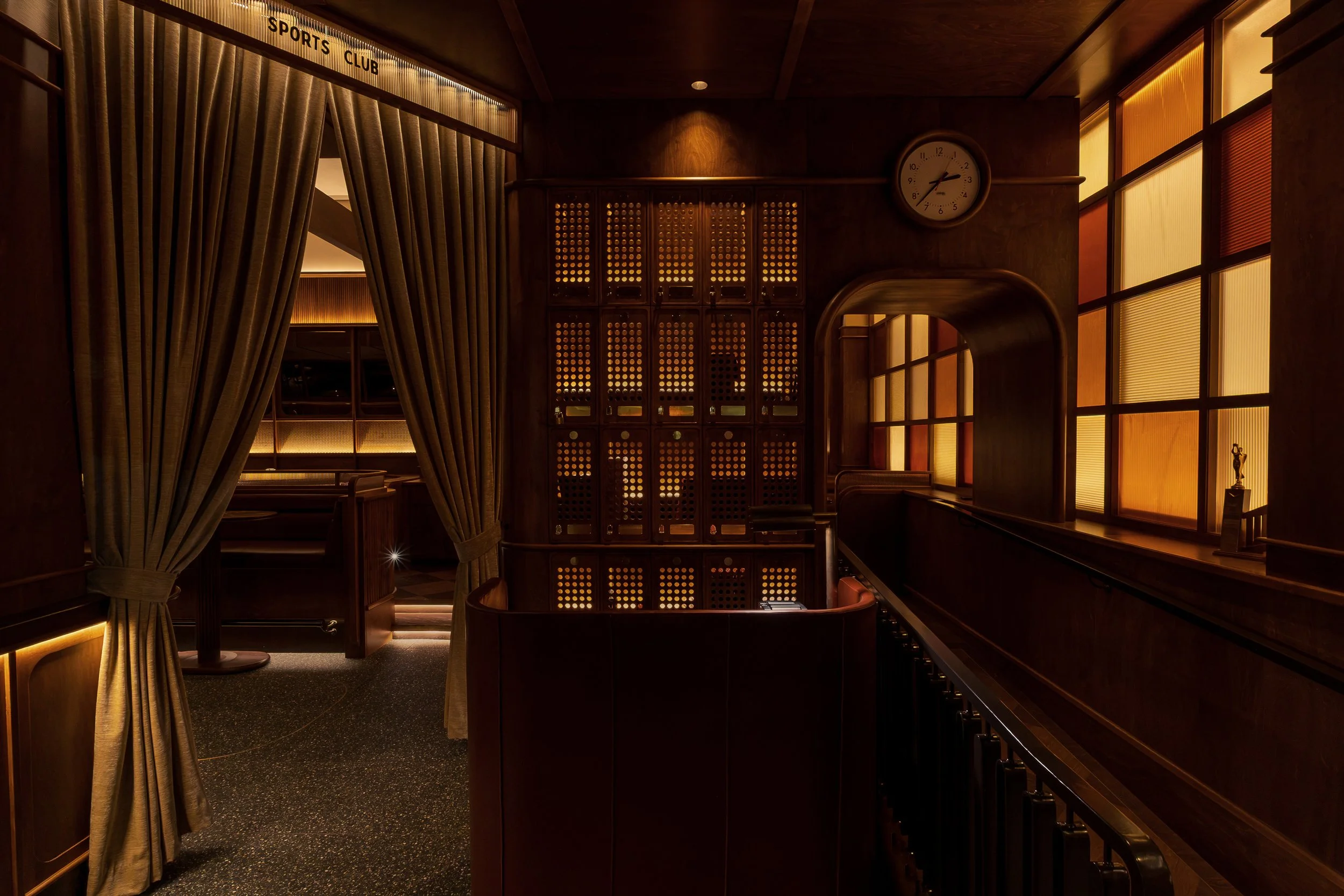 Custom metal screens, integrated display niches and a vintage-style wall clock define a layered transition within Austin Sports Club.