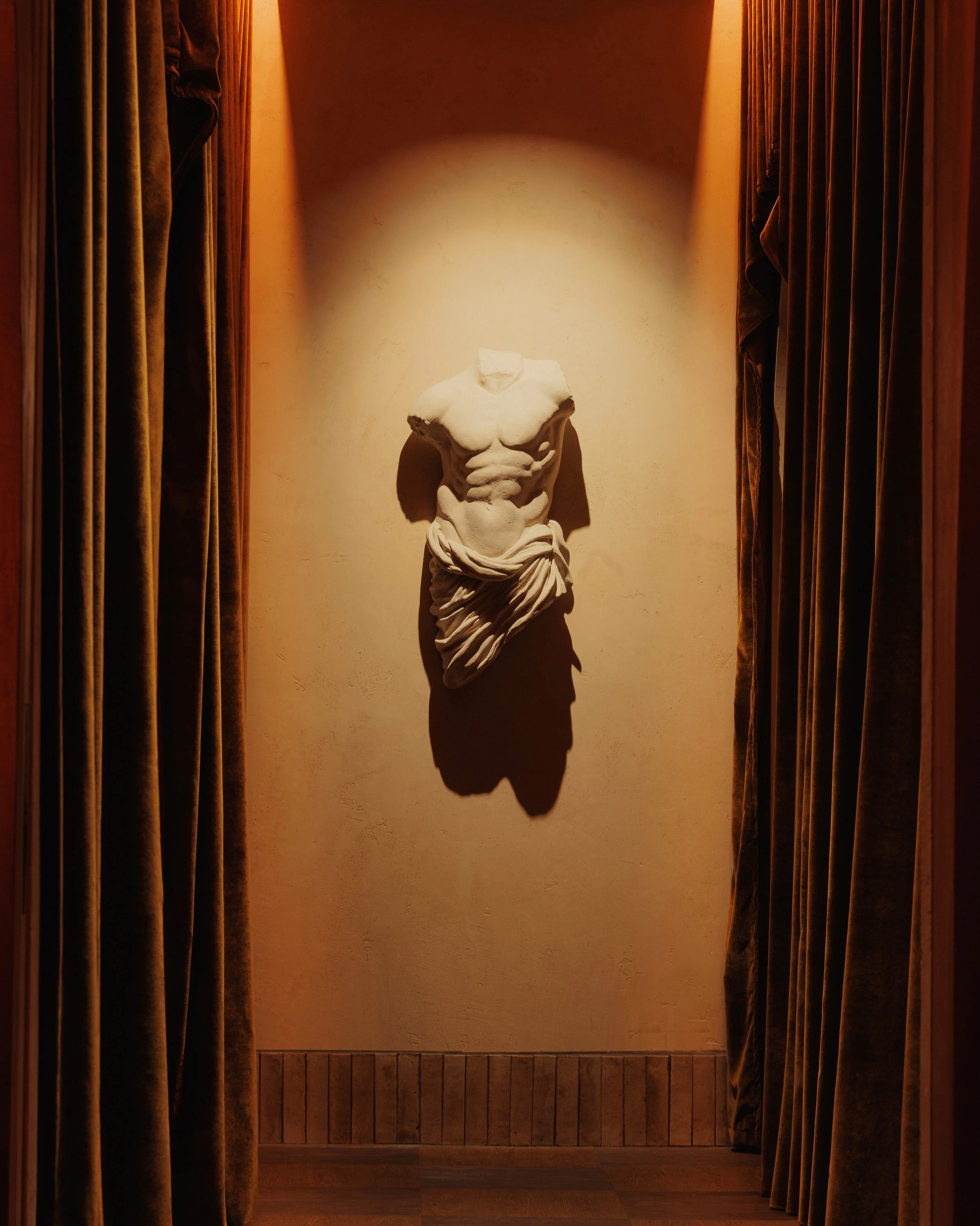 Headless classical torso dramatically illuminated within a narrow curtained niche at Roman God of Fire in Tempe.