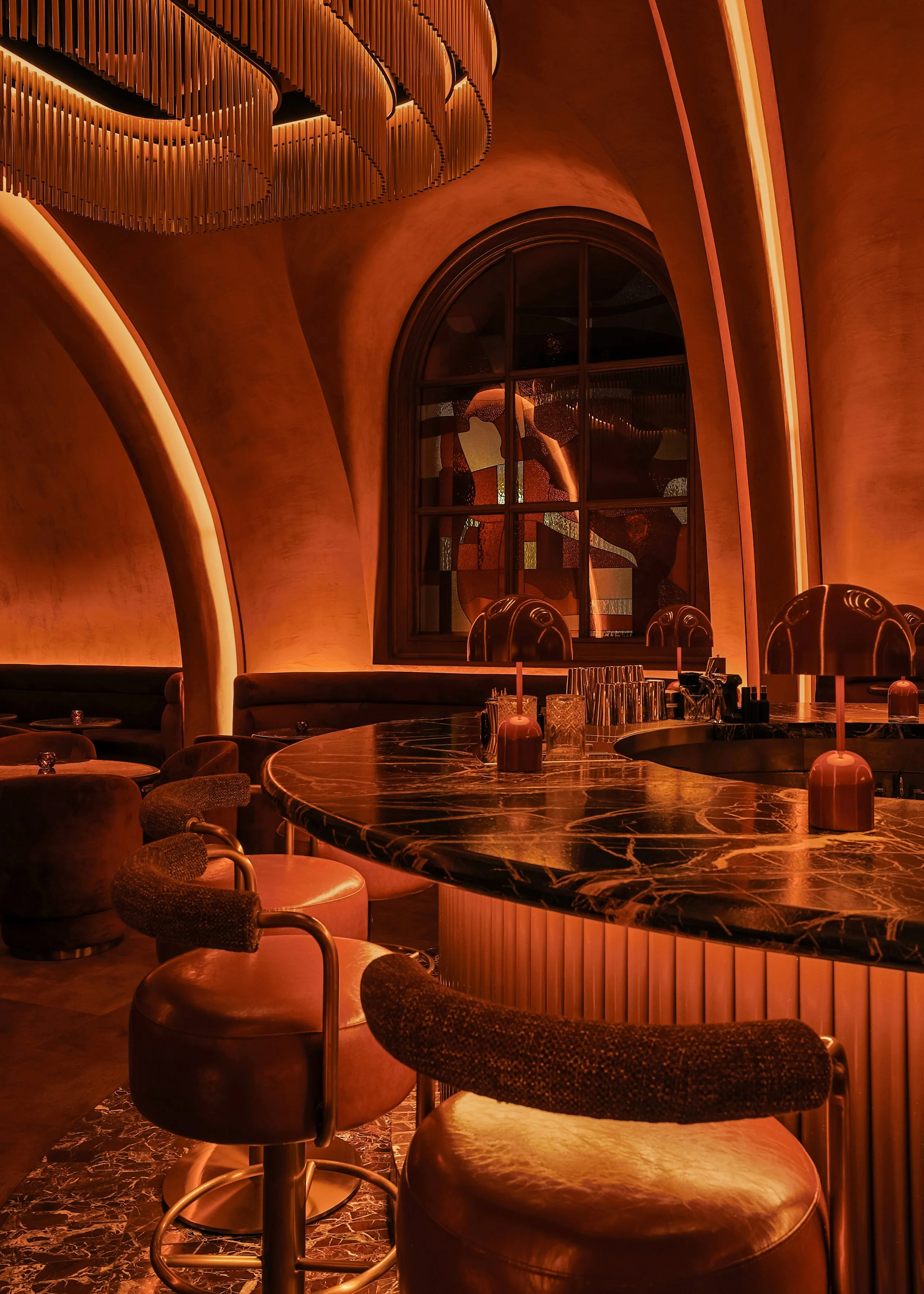 Close view of Mea Culpa’s marble bar, fluted illuminated base, upholstered stools and distinctive red dome lamps beneath a glowing vaulted arch.