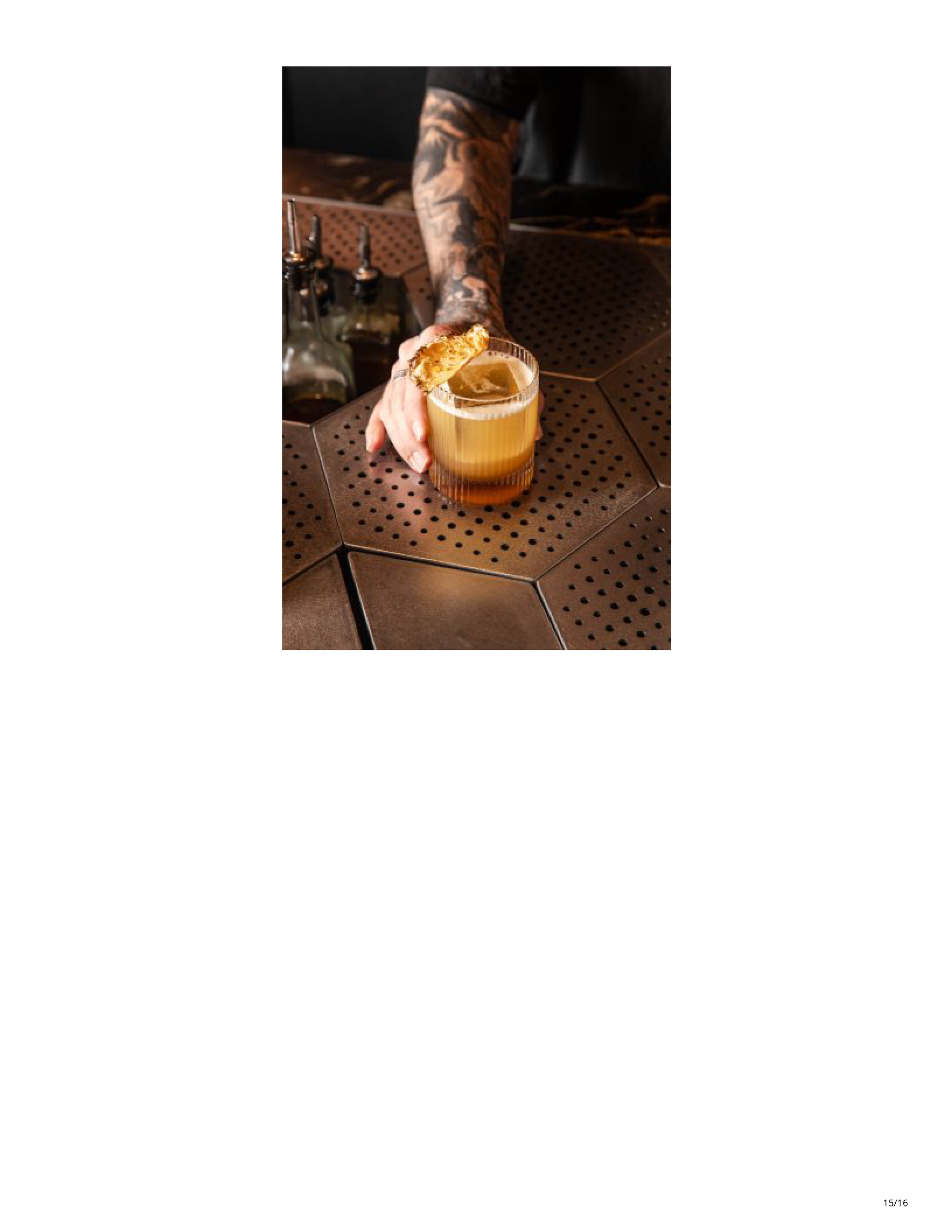Bartender presenting a golden cocktail on the geometric metal bar surface at Drop Dead Gorgeous.