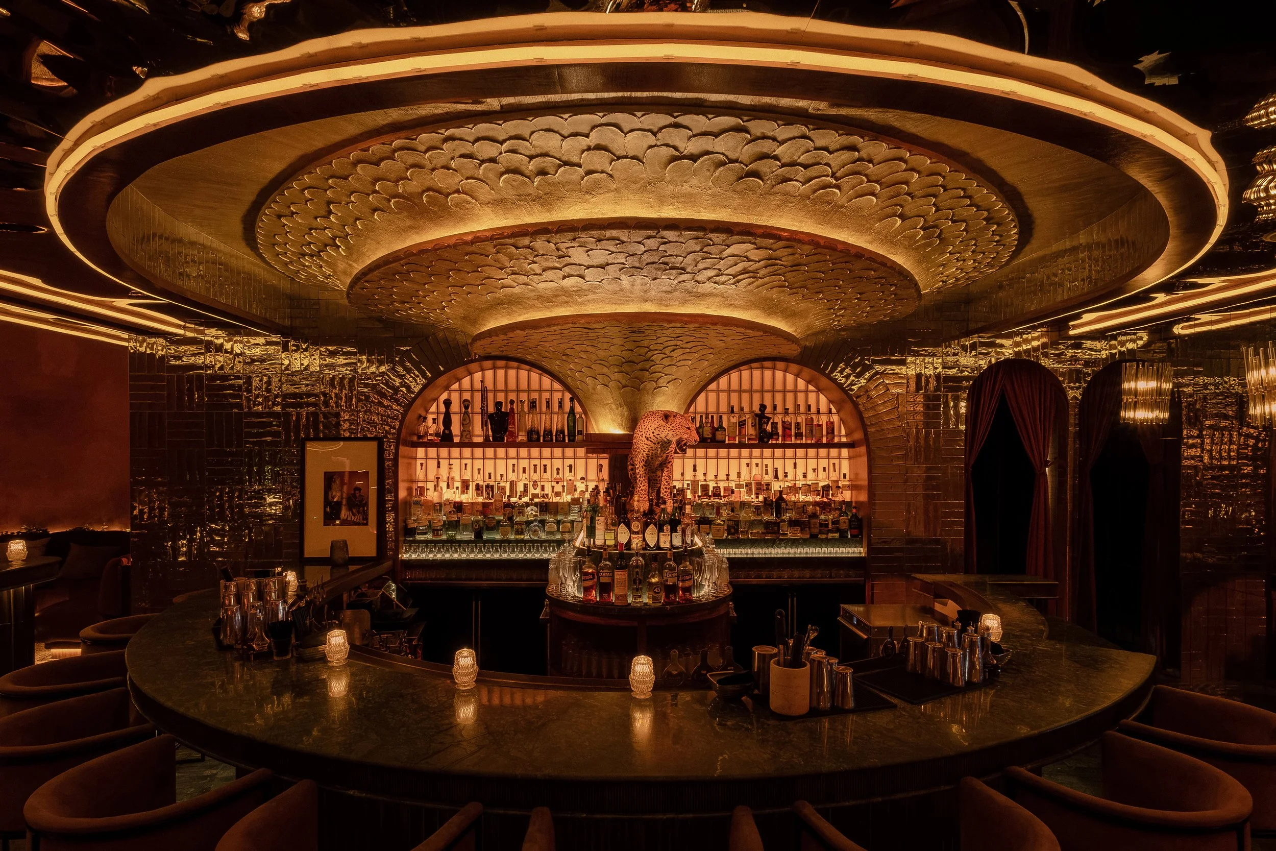 Symmetrical view of Powder Room’s circular bar beneath an ornate concentric ceiling illuminated with warm concealed lighting.