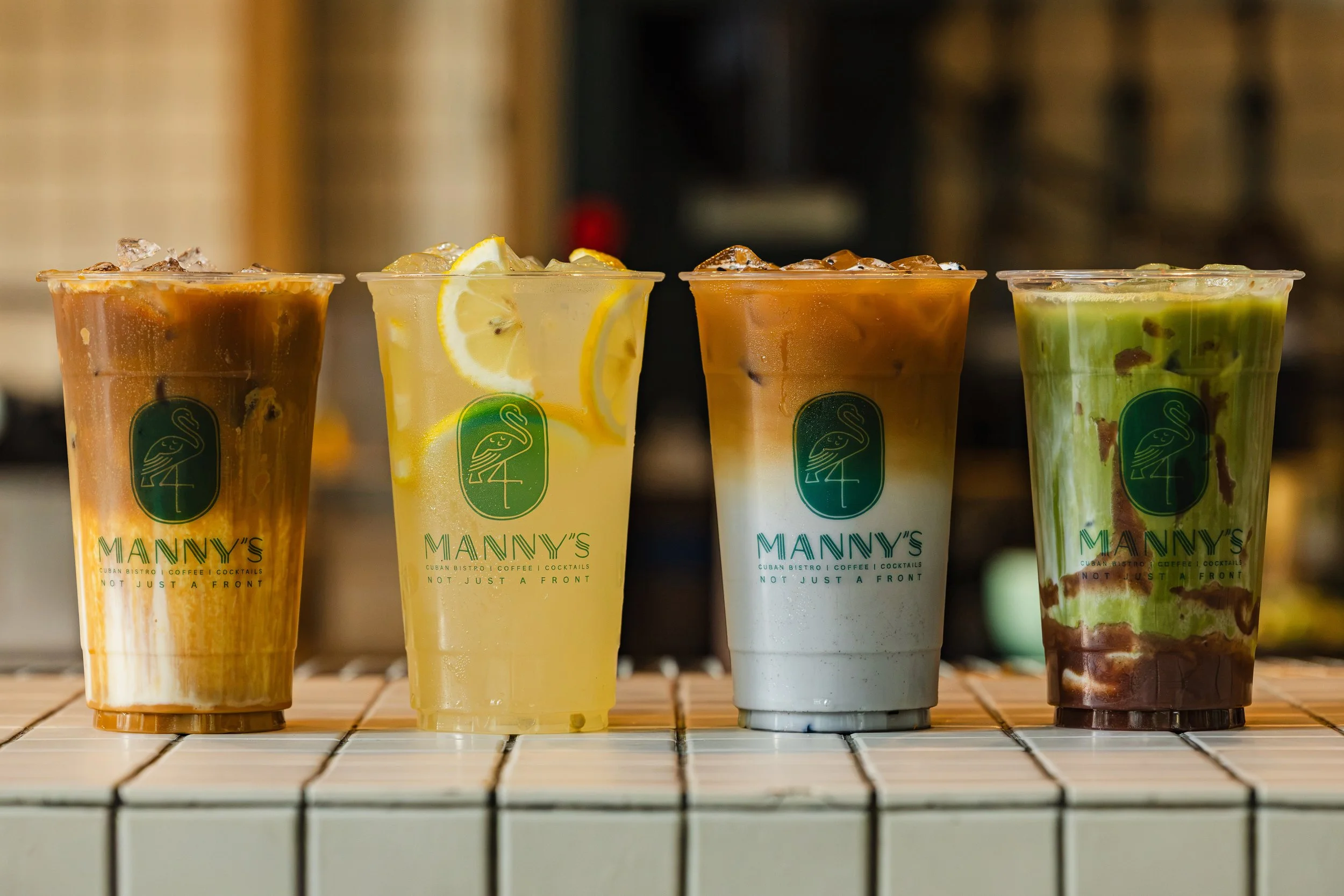 Close-up of four colorful specialty drinks displayed along the tiled bar counter at Manny’s.