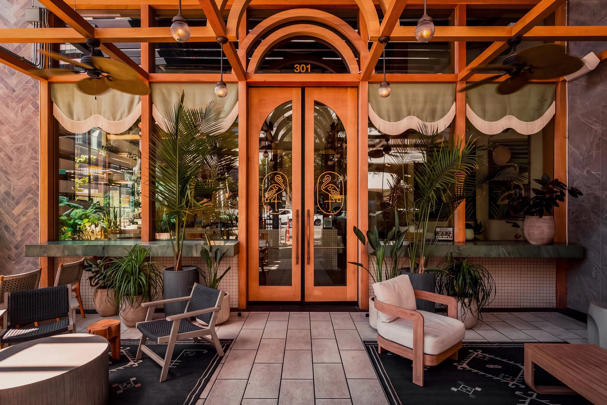 Arched glass entrance to Manny’s in downtown Austin, surrounded by tropical plants and outdoor lounge seating.