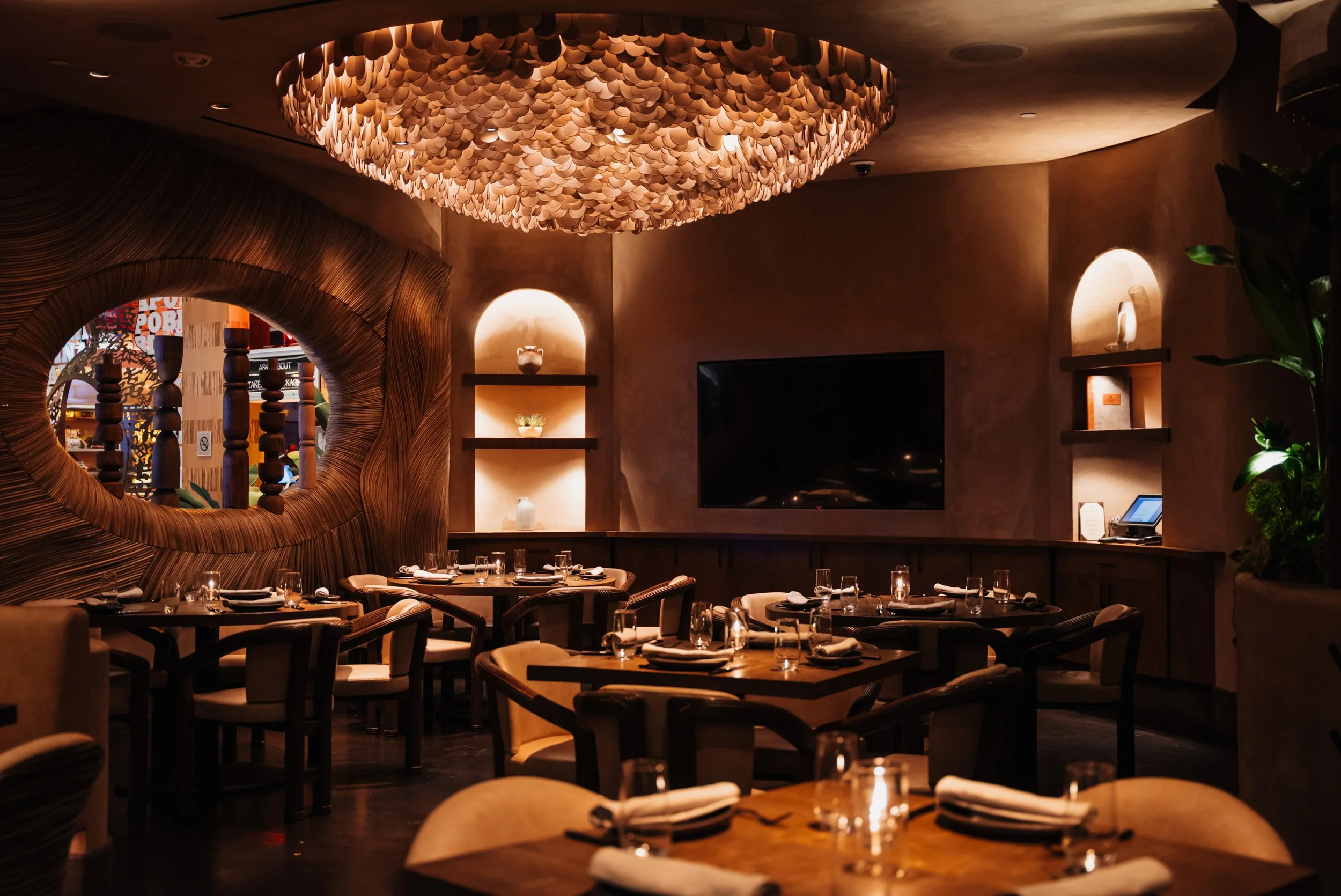 Amaya Modern Mexican restaurant interior at The Cosmopolitan of Las Vegas, featuring a warmly illuminated bar, wood ceiling, sculptural pendant lights, intimate dining tables, and lush planting.